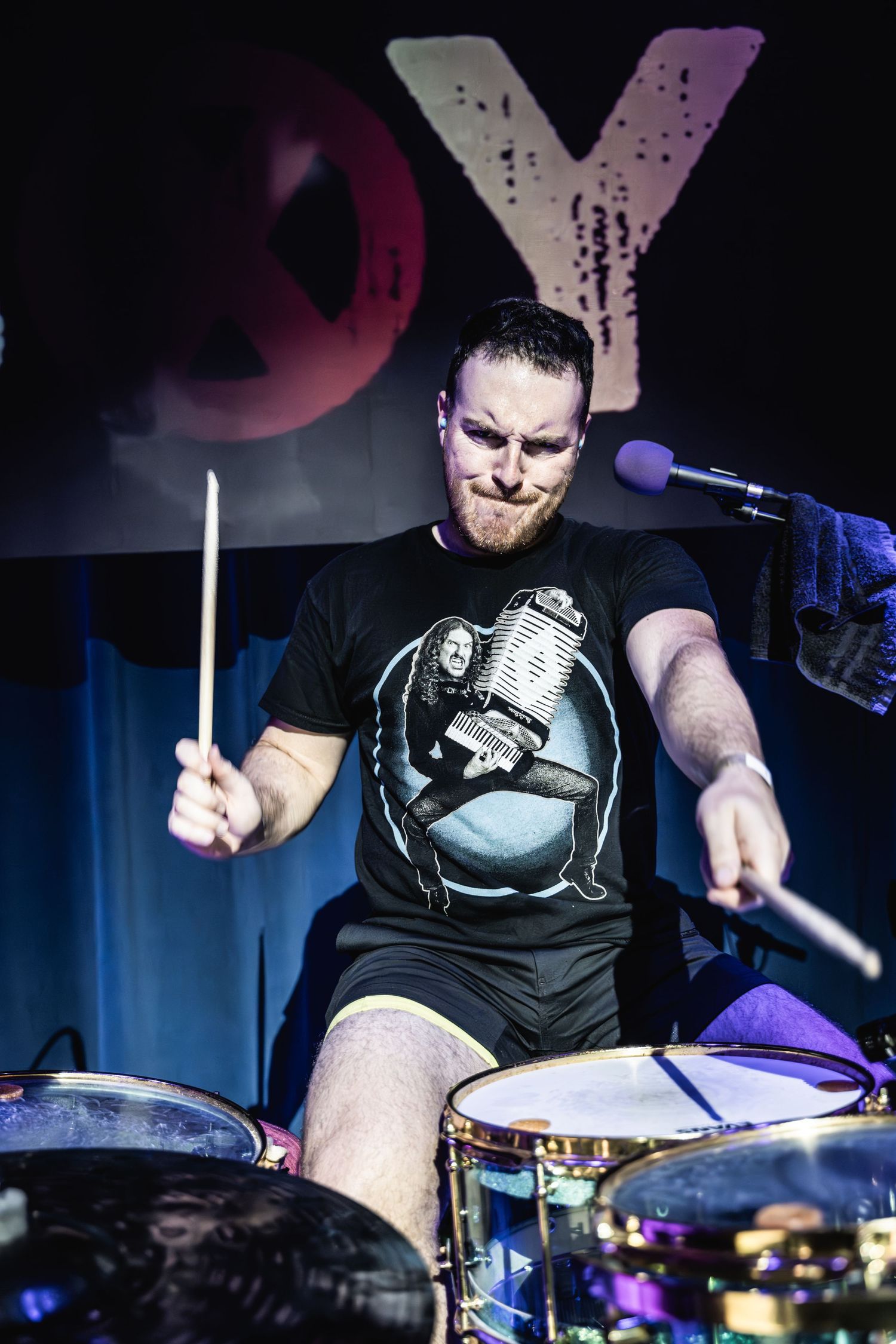 Energetic drummer performing on stage with drumsticks in hand under dramatic lighting.