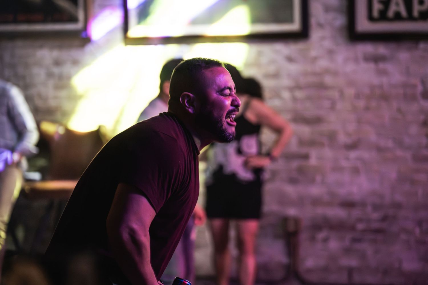 Performer singing passionately on stage with dramatic lighting against brick wall backdrop.