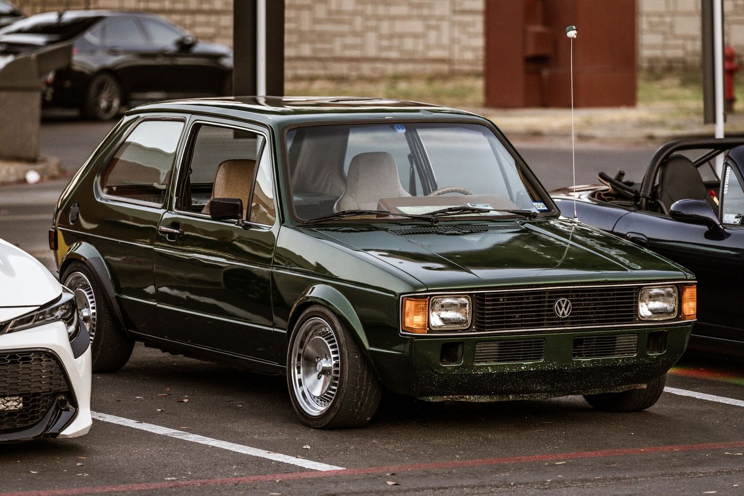 Lowered vintage black Volkswagen Rabbit with aftermarket wheels in a parking lot.