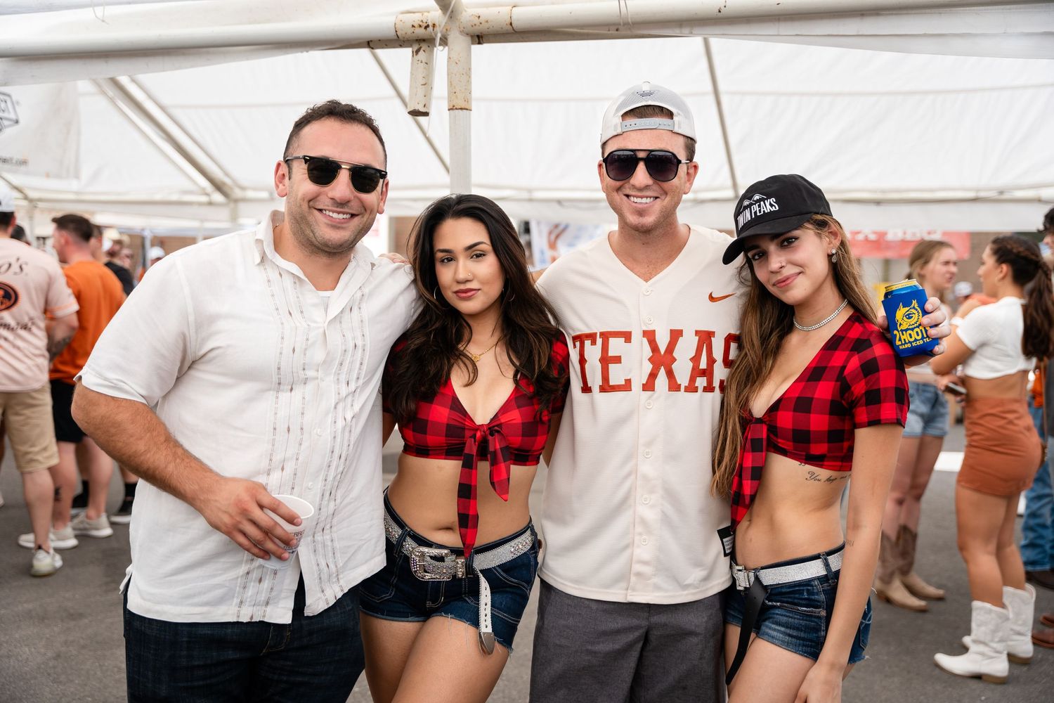 Group of friends in casual attire pose together at outdoor Texas sporting event.