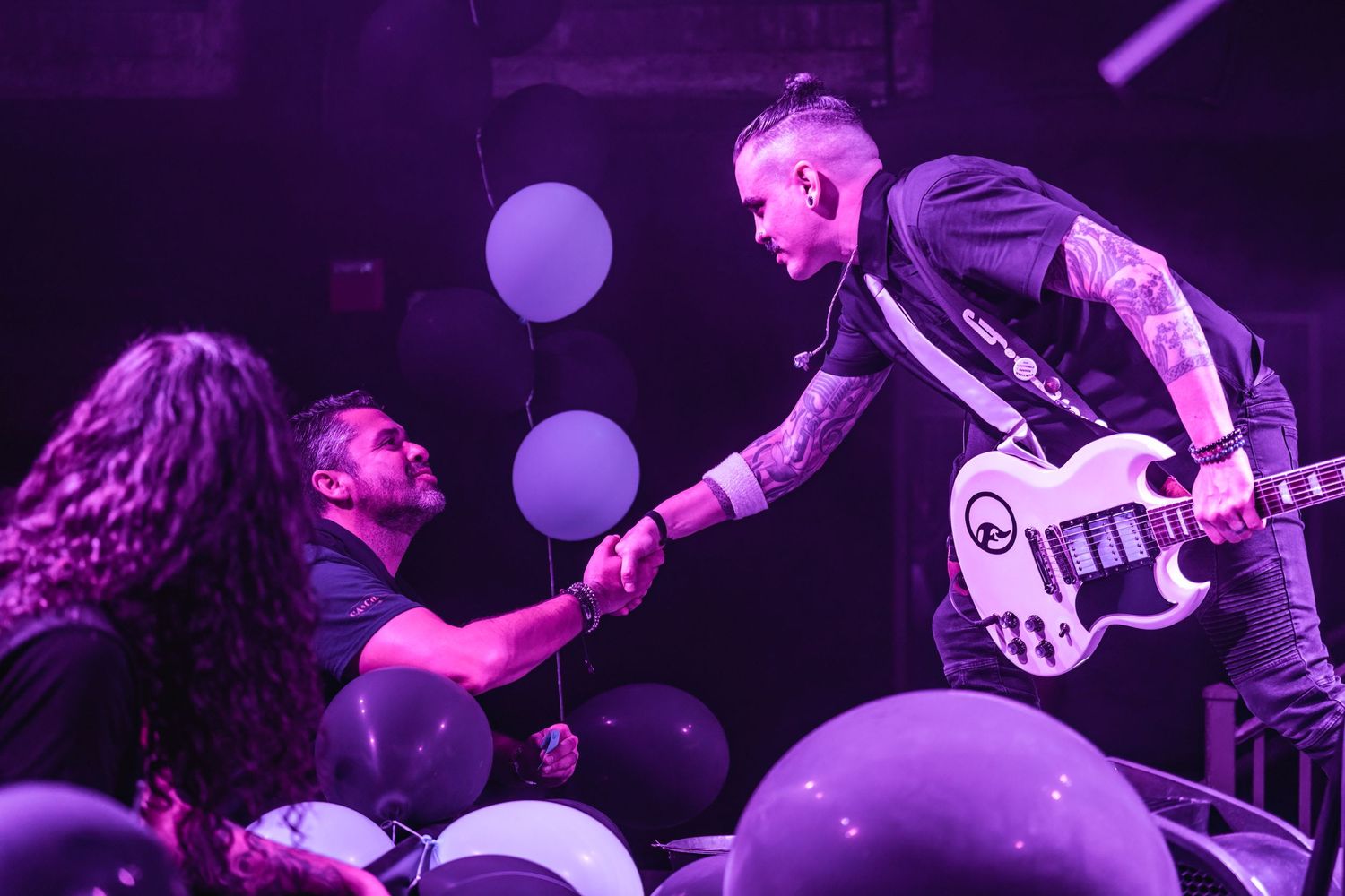 Musicians interact with audience during concert performance with purple lighting and floating balloons.