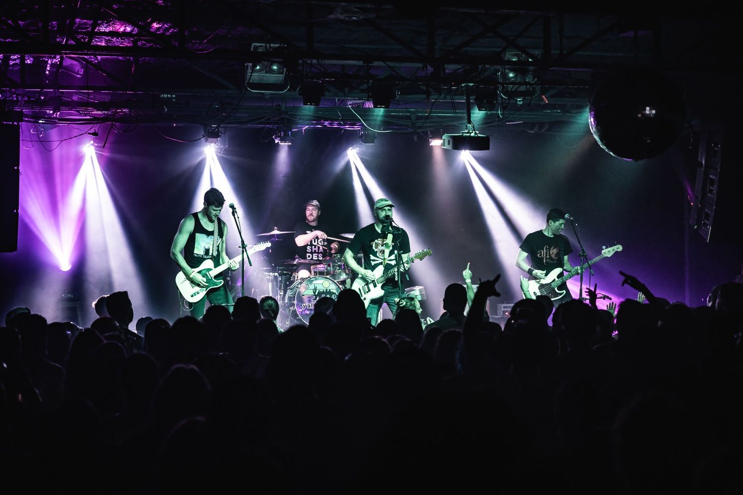 Rock band performs on stage with dramatic white spotlights and silhouetted crowd.