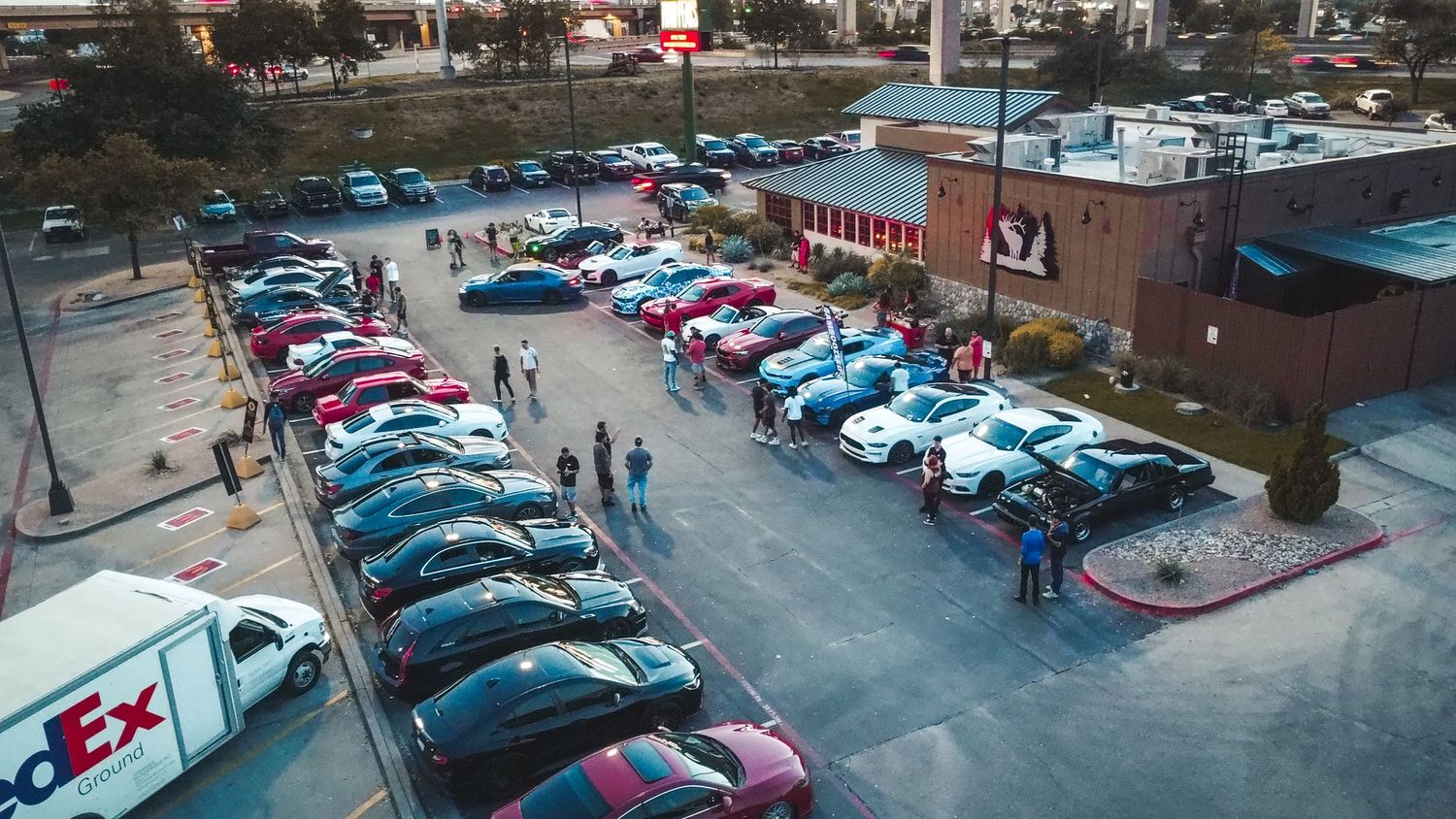 Aerial view of a car meet showing rows of parked vehicles in a lot at dusk.