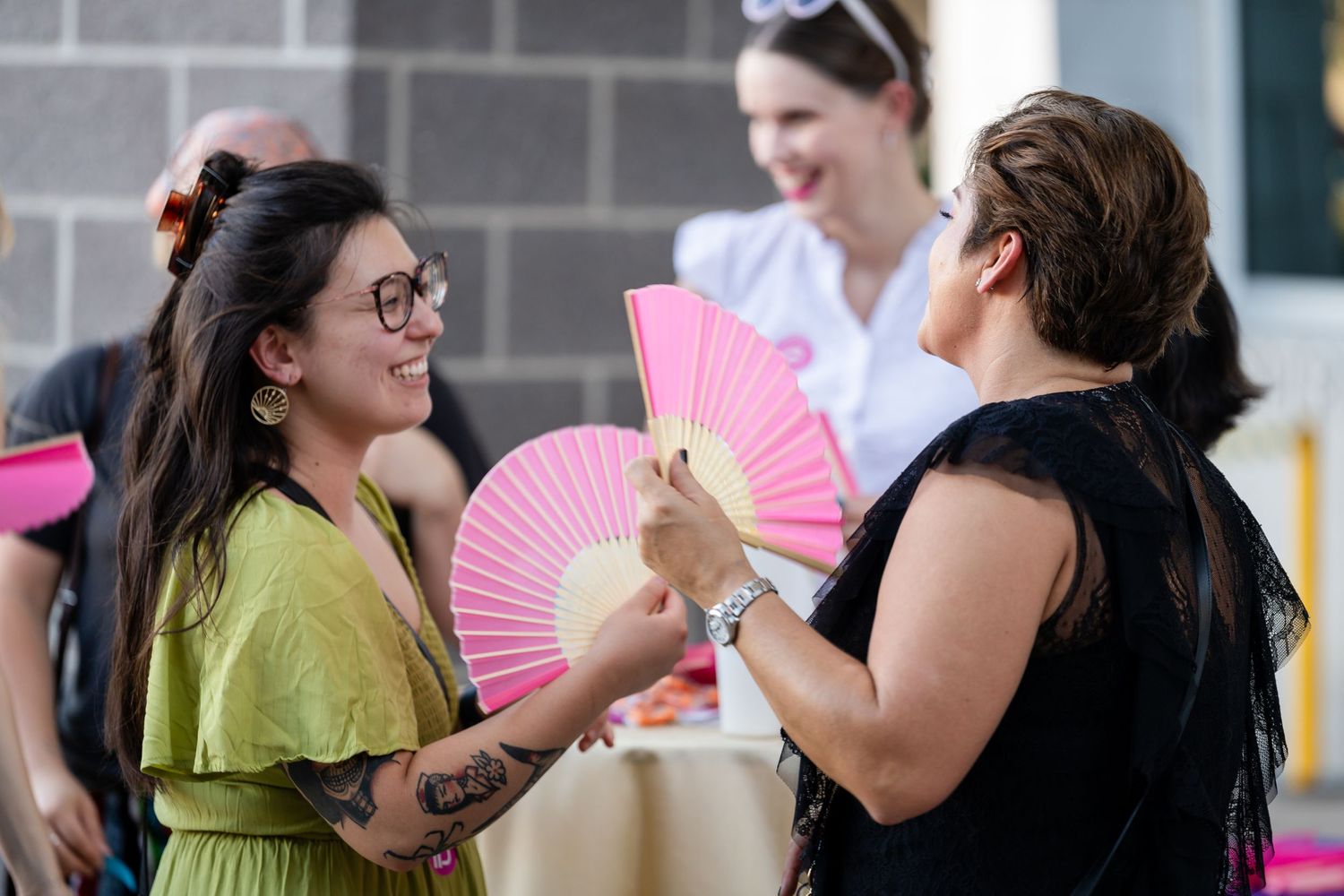 People sharing pink paper fans at an outdoor summer event.
