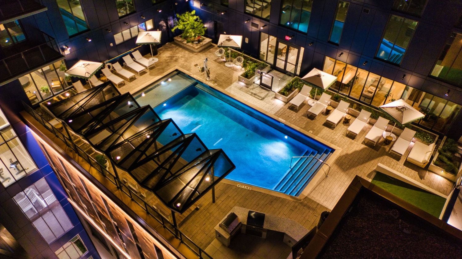 Aerial view of luxury rooftop swimming pool with modern loungers and ambient lighting at night.