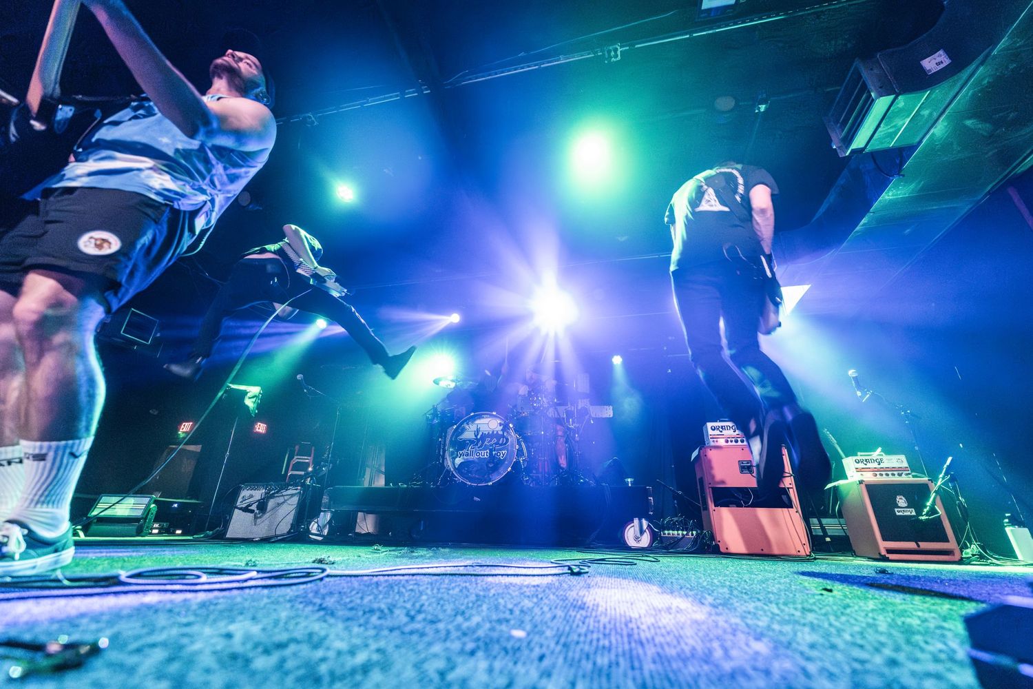 Concert performers jumping on stage with dramatic blue and green lighting effects during an energetic live show.