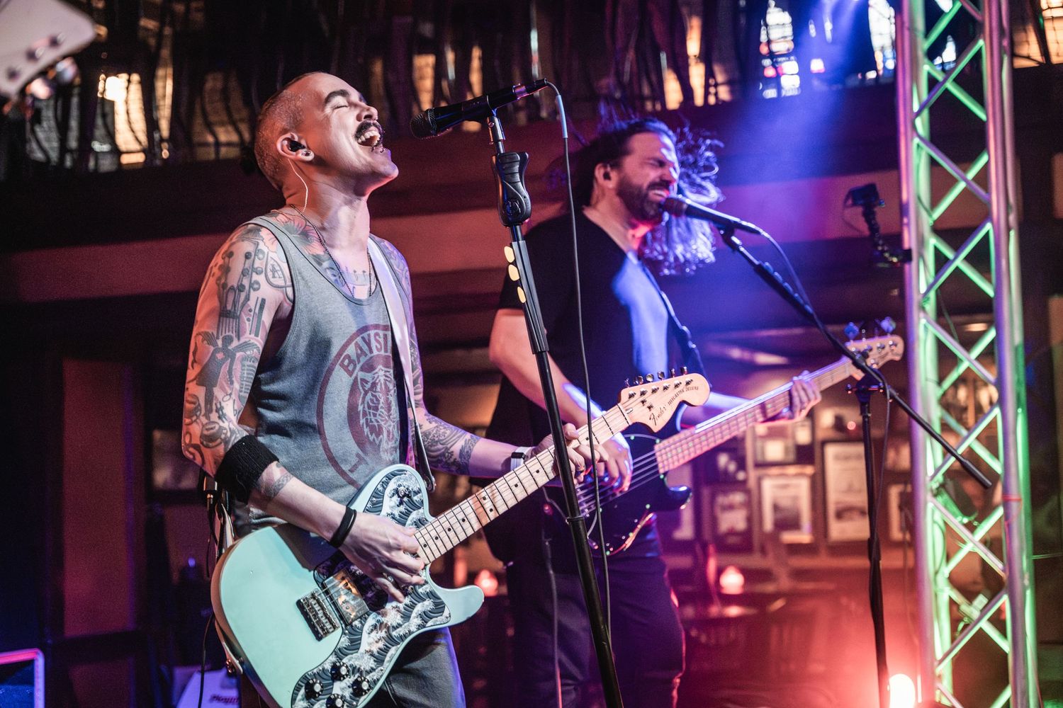 Musicians perform energetically on stage with a mint green guitar under dramatic concert lighting.