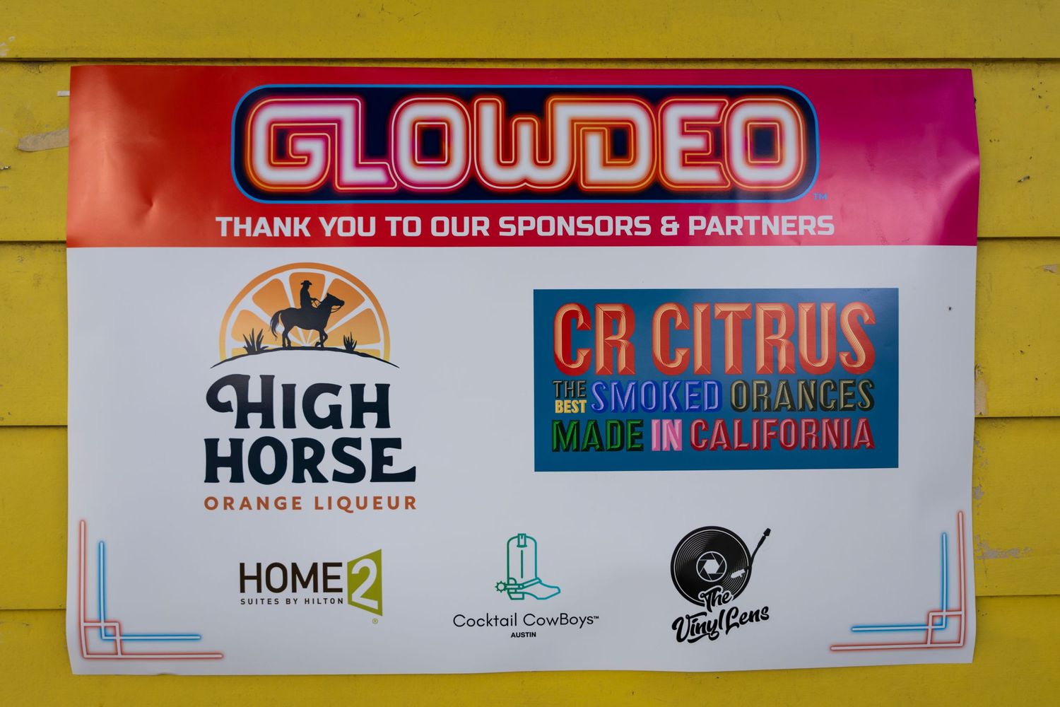 A sponsor board featuring Glowdeo event partners including High Horse brand and CR Citrus logos against a yellow wall.
