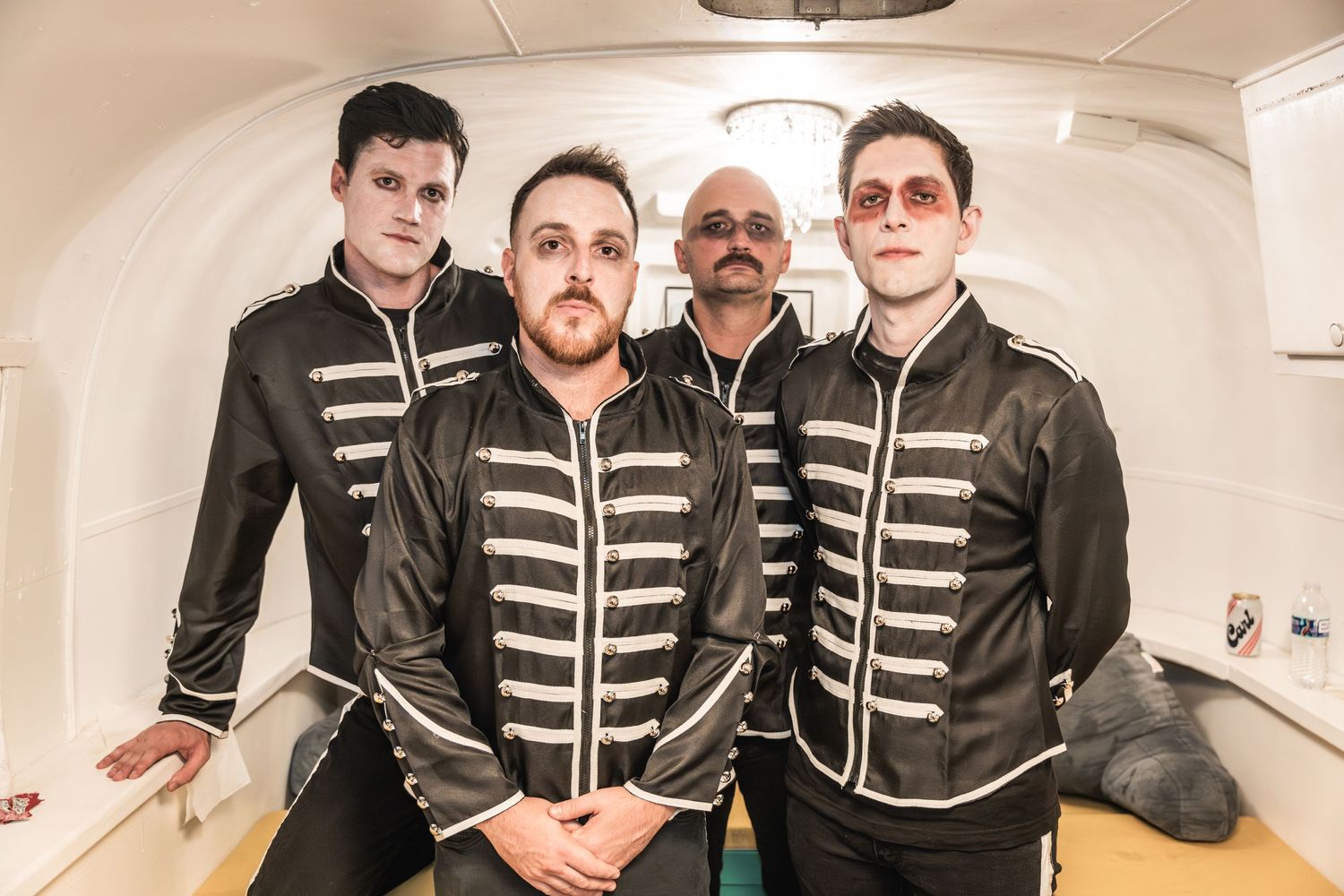 Band members in matching striped military jackets pose in what appears to be a backstage area.