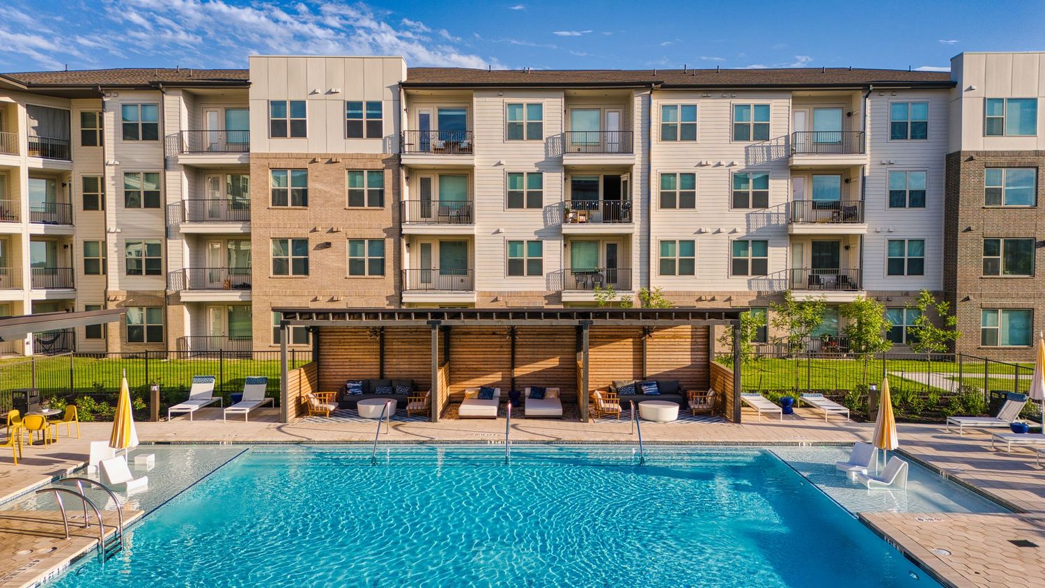 Luxury apartment building with swimming pool and wooden pergola surrounded by lounge chairs.