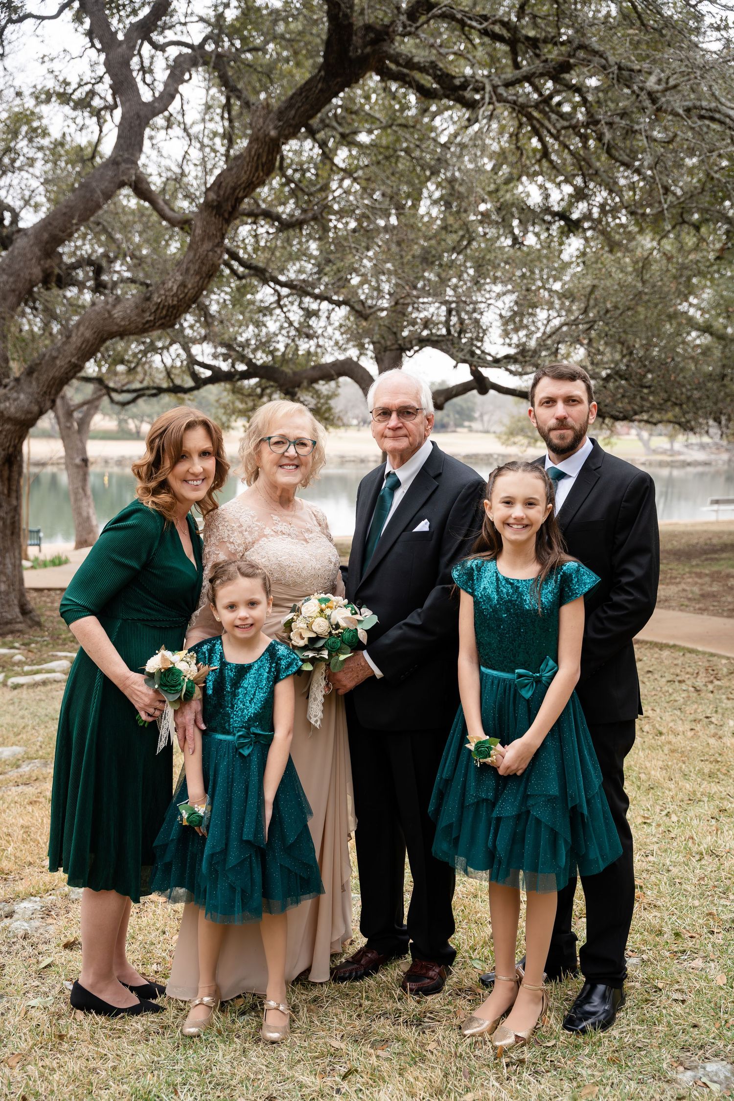A family portrait taken outdoors with people wearing formal attire in emerald green dresses and dark suits.