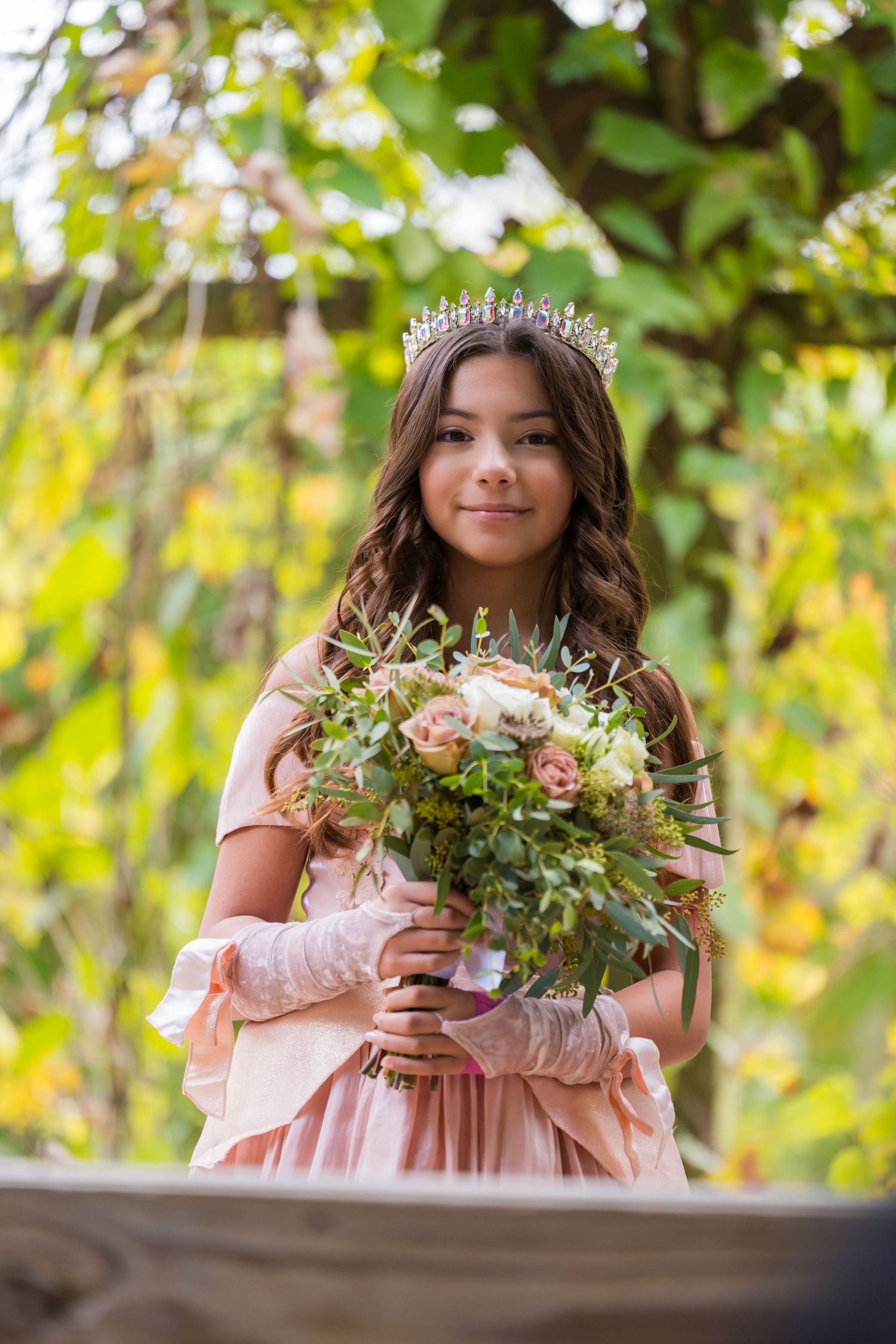 A princess in a pink dress holding a floral bouquet poses against autumn foliage.