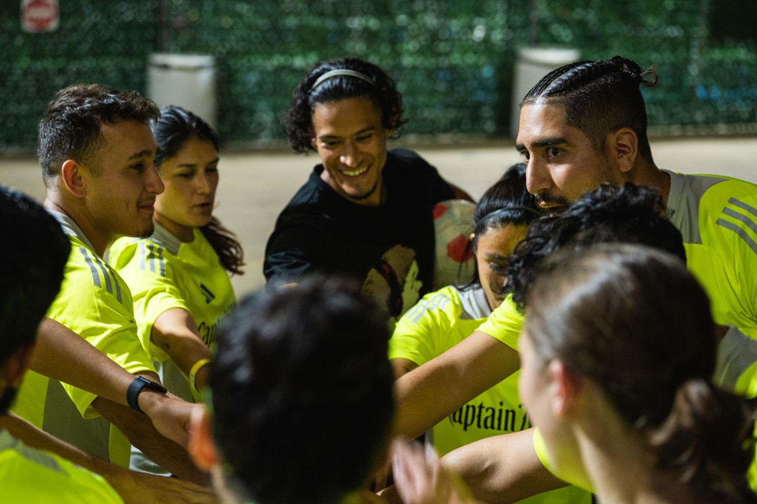 Soccer team huddle during nighttime practice wearing bright yellow uniforms.