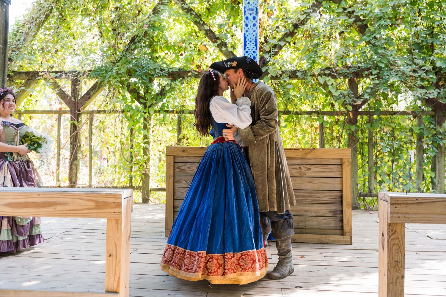 Couple in renaissance costumes share romantic moment during wedding ceremony on outdoor wooden stage.
