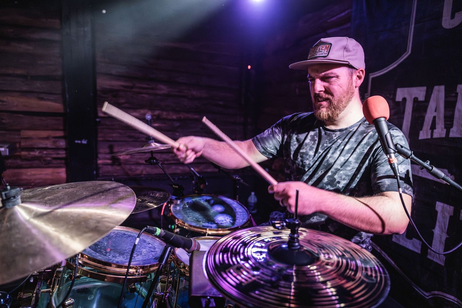 Drummer playing cymbals with intense focus under blue stage lights.