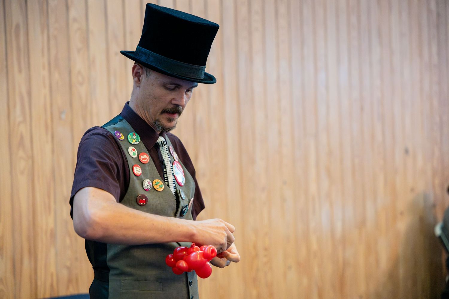 Performer in top hat and vest skillfully manipulates red juggling balls during an entertainment show.