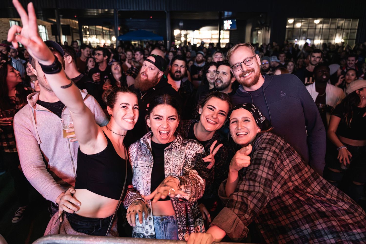 Concert crowd poses together at music venue with stage lighting in background.
