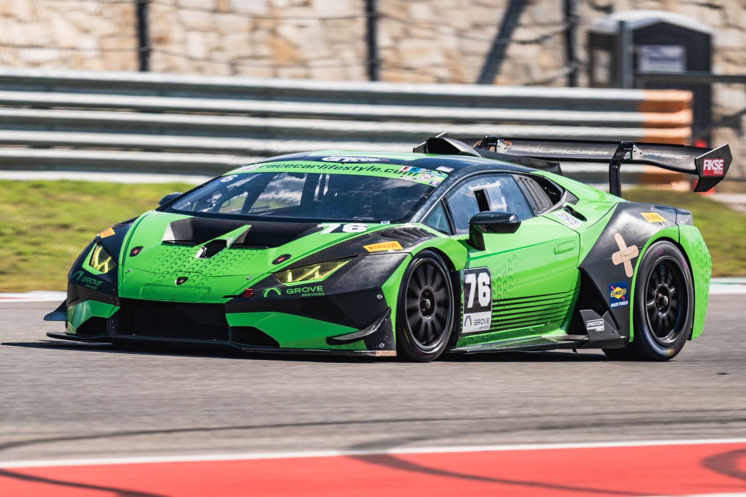 Bright green Lamborghini GT3 race car speeds through a turn on a professional racing track.