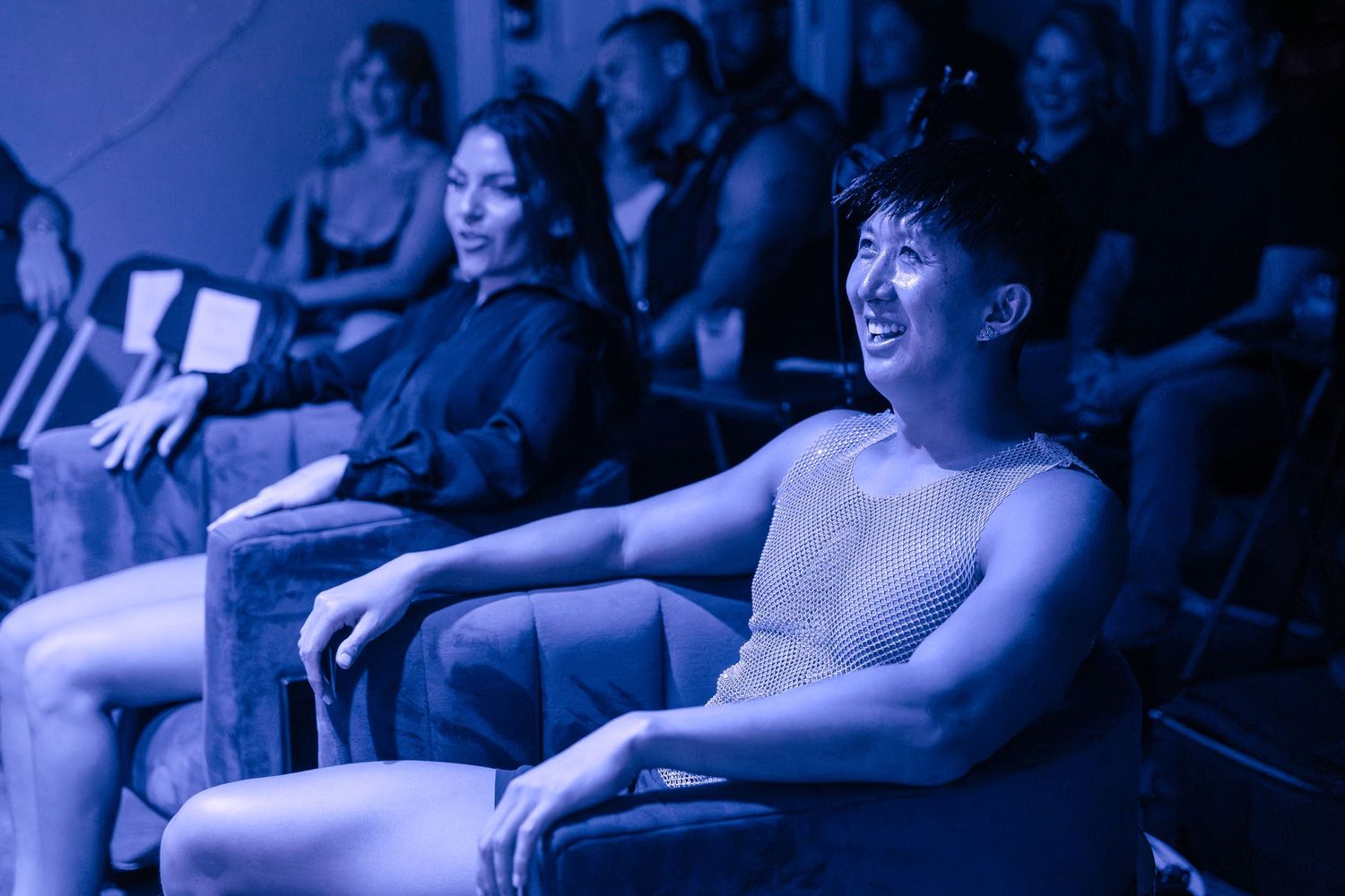 Theater audience members sit in darkness illuminated by blue stage lighting.