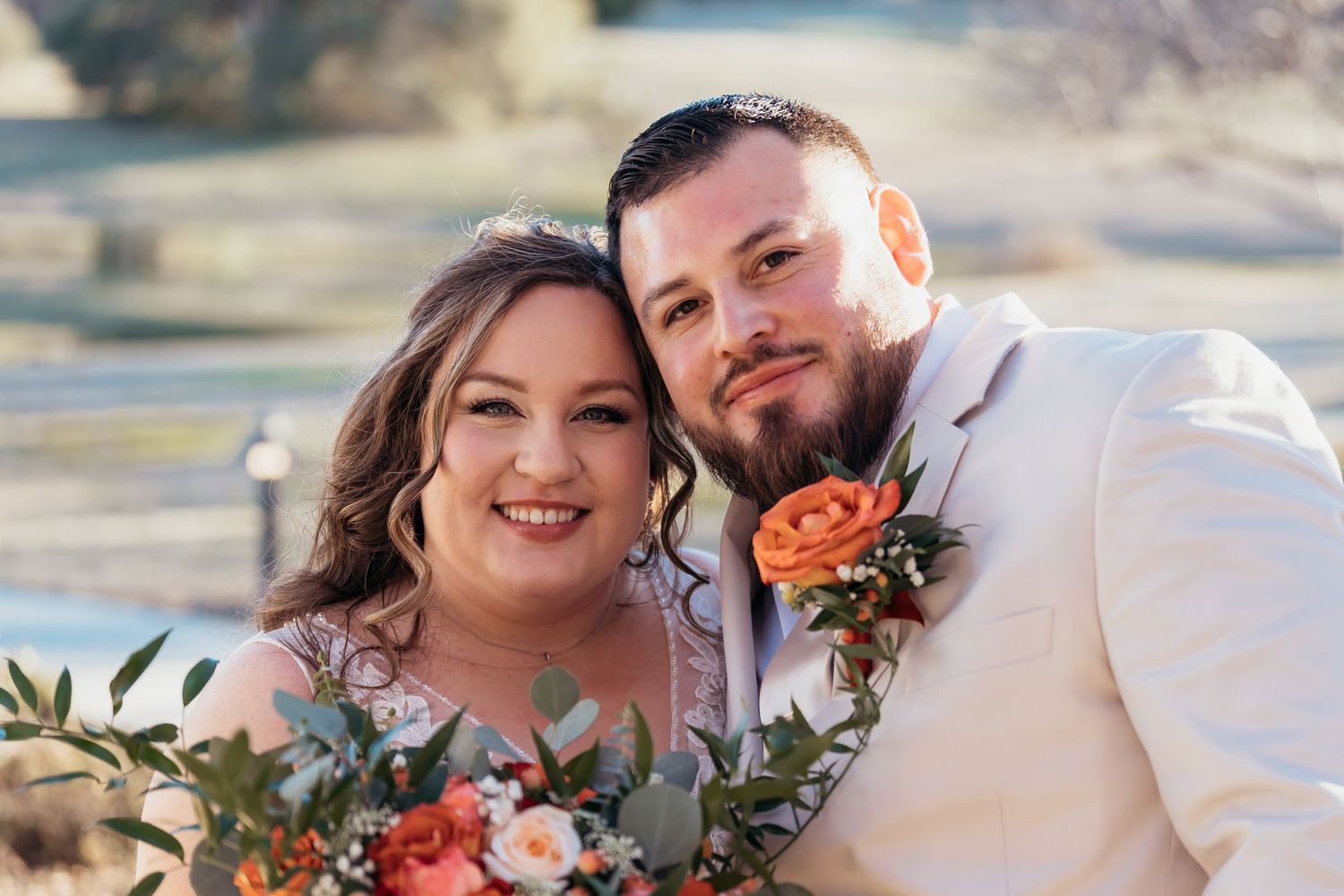 A romantic outdoor wedding portrait with coral roses and greenery bouquet.