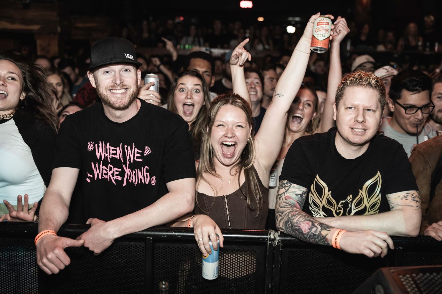 Concert crowd cheering and celebrating behind a security barrier at a live music event.