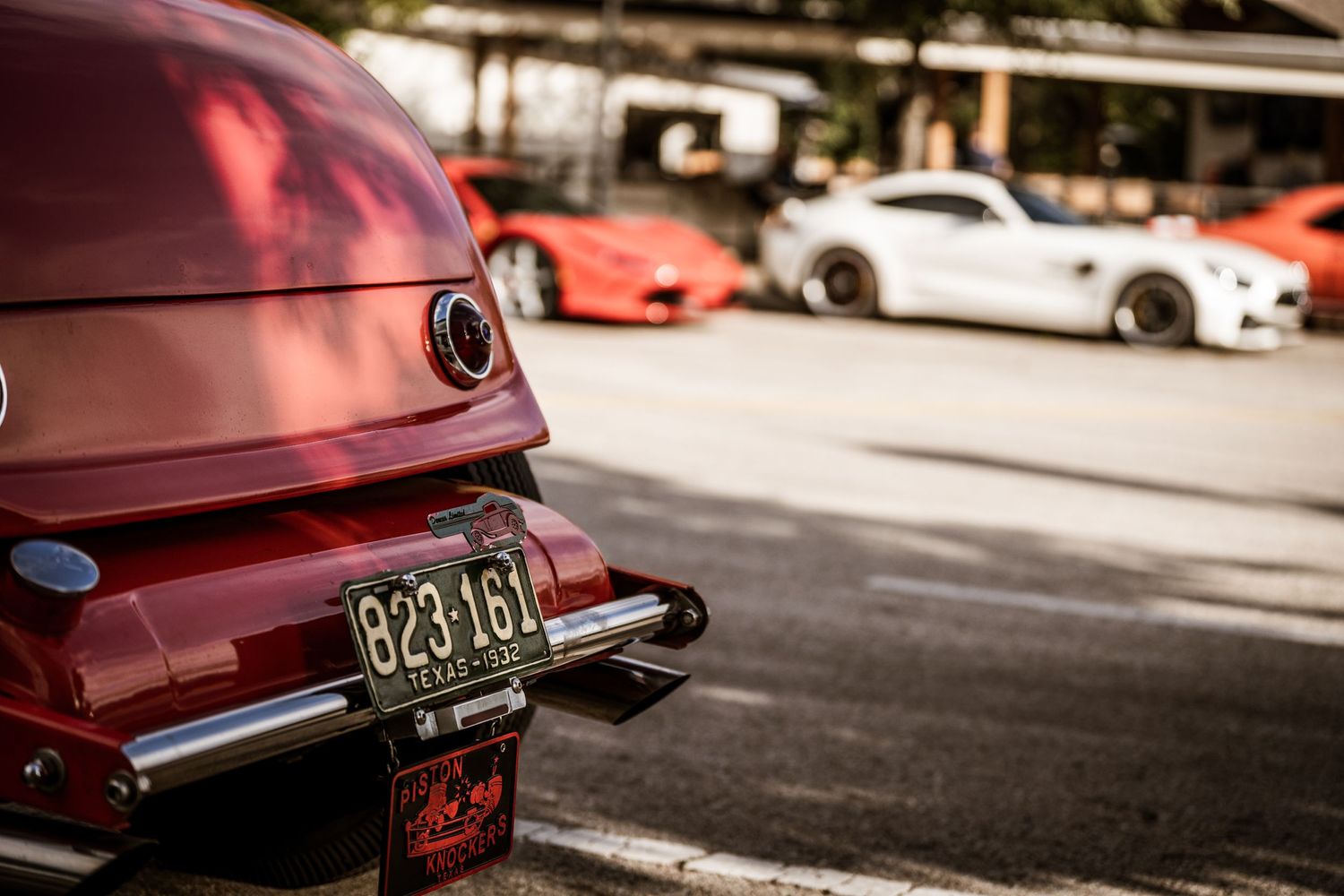 Rear view of burgundy classic car with visible license plate in parking lot.