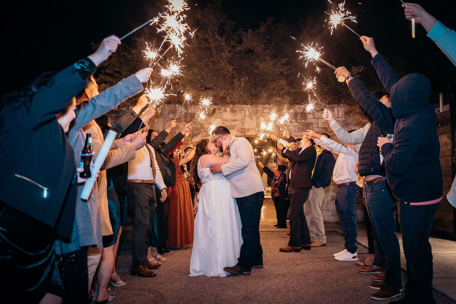 Newlyweds sharing a romantic moment under a sparkler sendoff at night.
