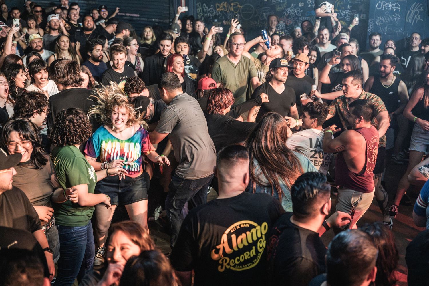 Energetic crowd of concert-goers enjoying live music in a dark venue with bodies packed together on the dance floor.