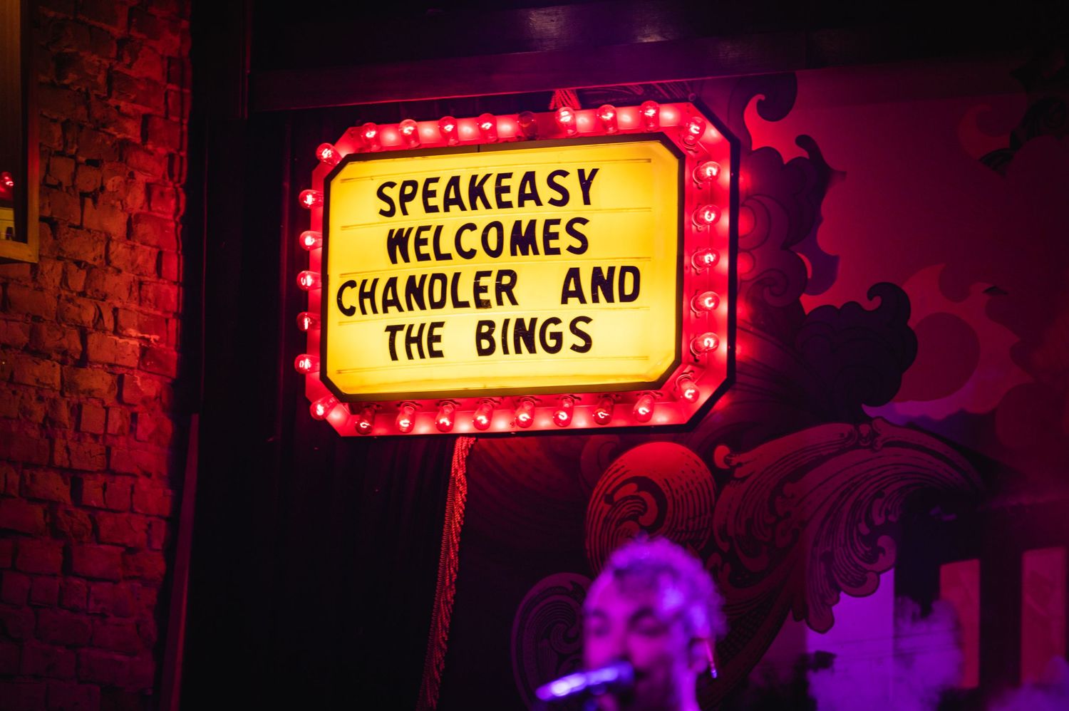 Illuminated venue sign reading 'Speakeasy Welcomes' with neon lighting.