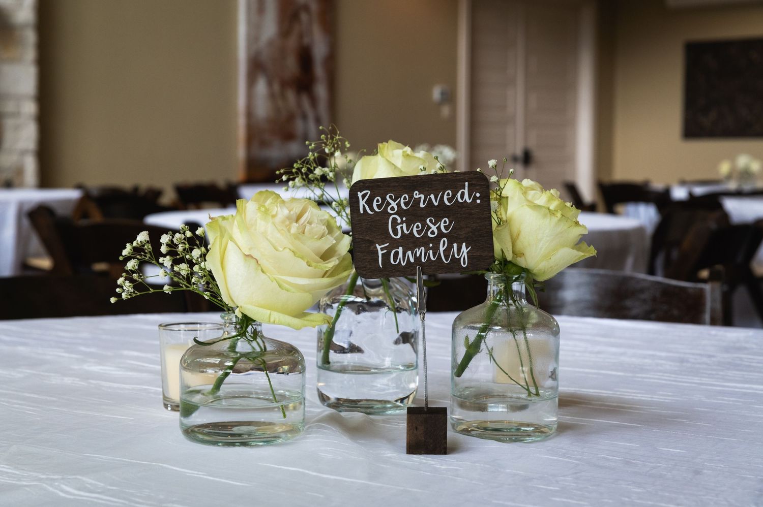Wedding table centerpiece with white roses in small vases and a Reserved sign.