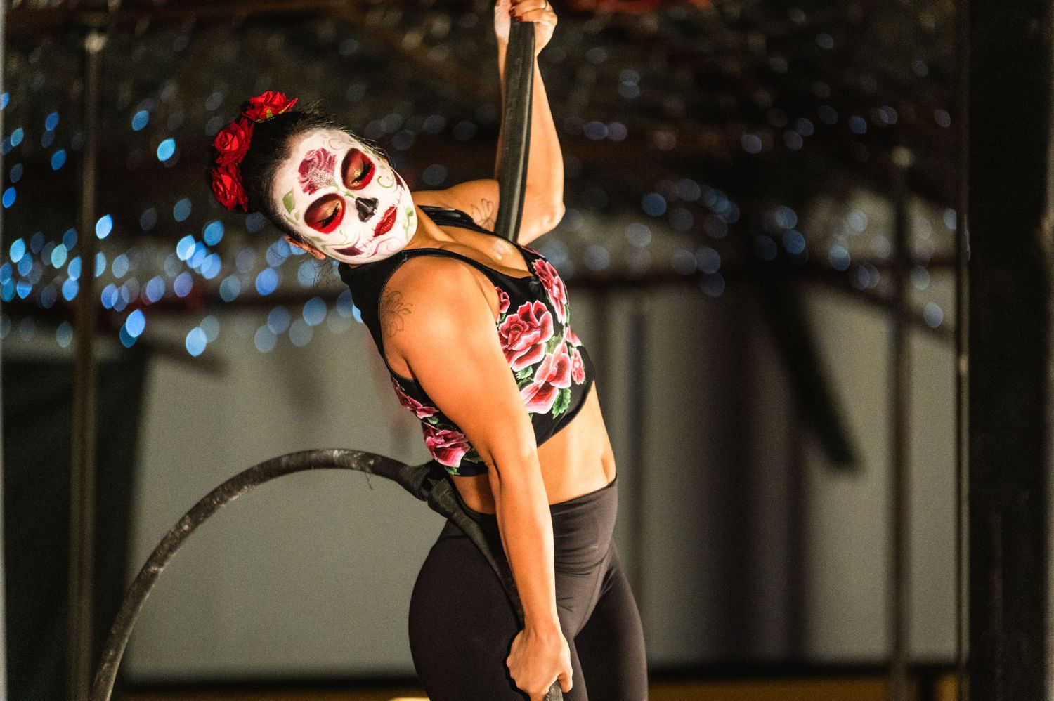Performer in dramatic makeup doing an acrobatic pose with twinkling lights in the background.