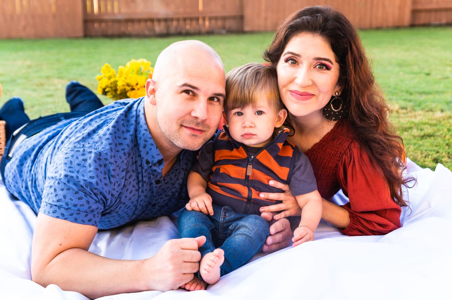 Family portrait on white blanket with yellow flowers in background.