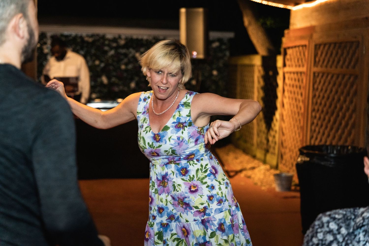 A person in a floral dress dances energetically at an evening celebration.