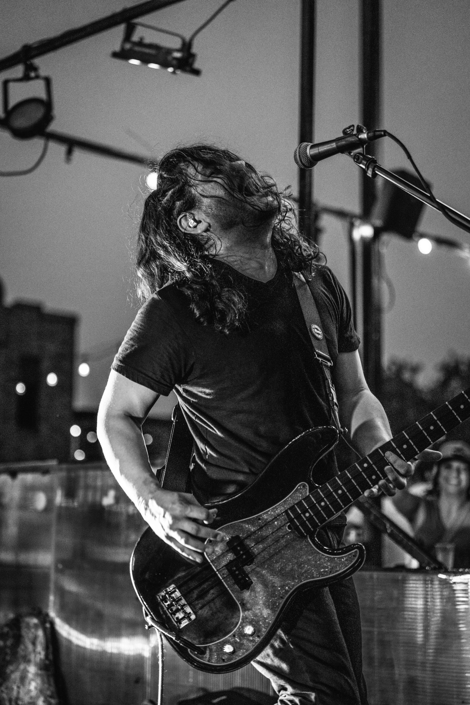 Bass guitarist performing intensely on stage in black t-shirt under dramatic stage lighting.