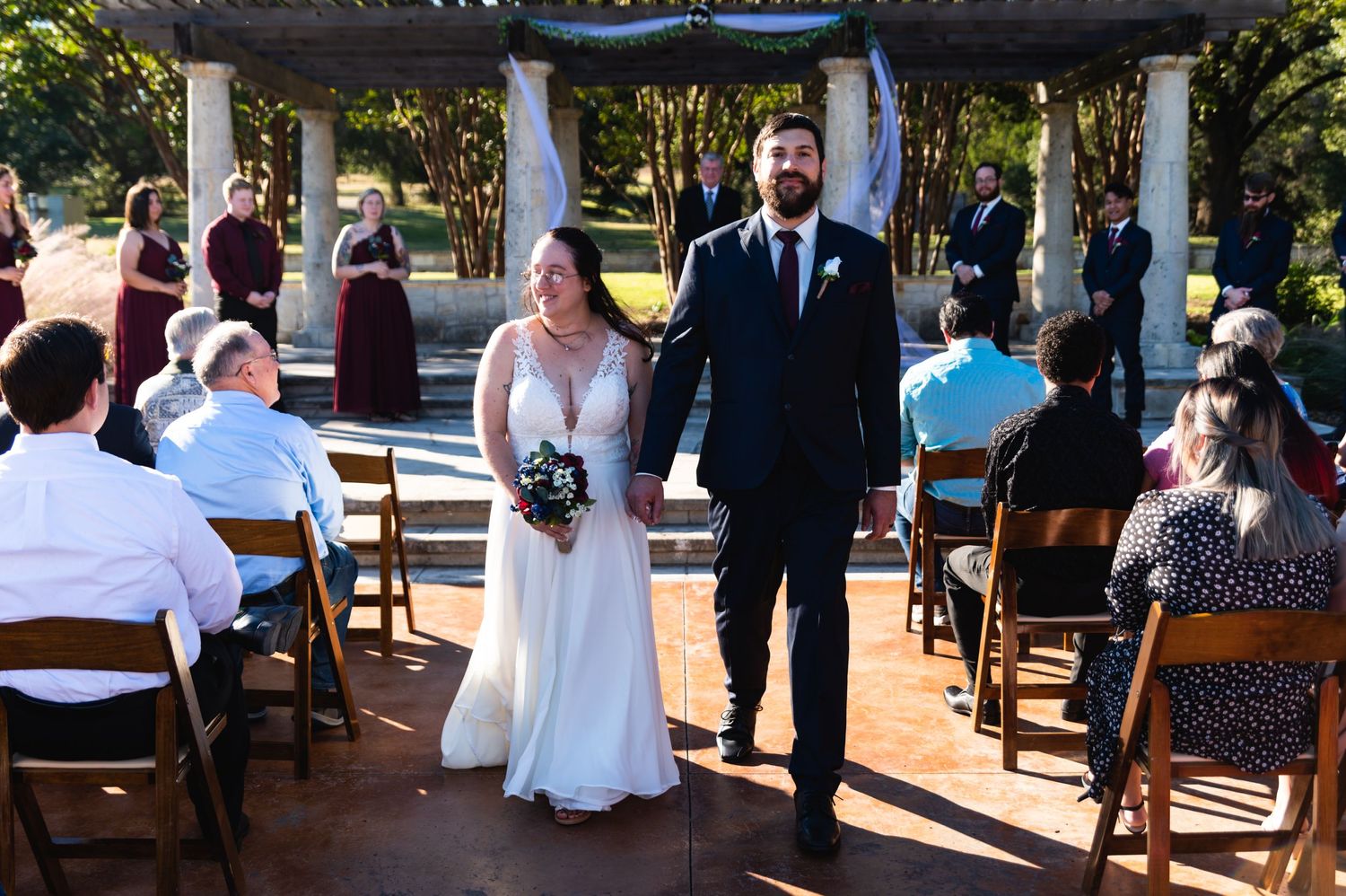 Bride and groom stand together at outdoor wedding venue with guests seated in background.