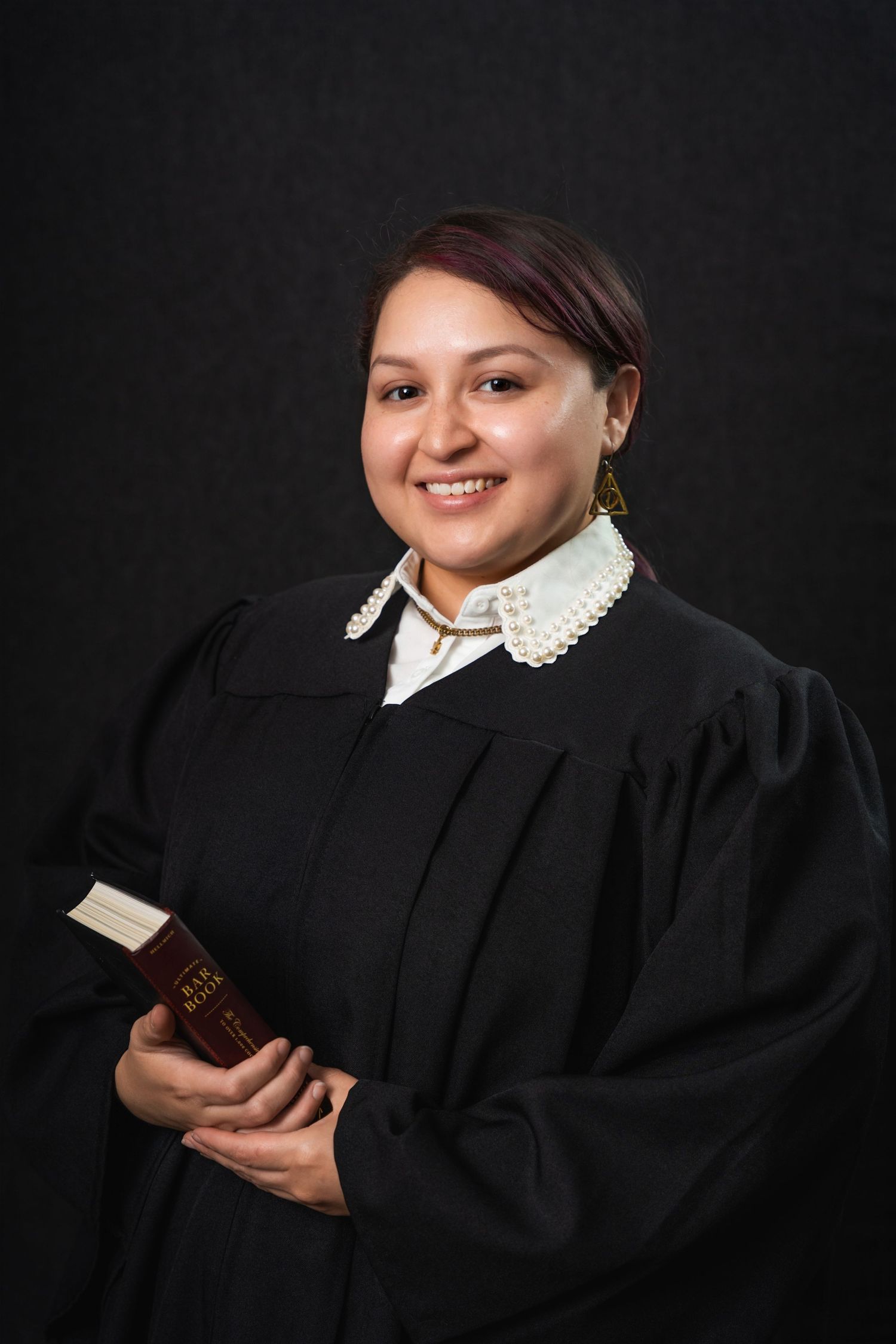 Judge wearing black robe and white collar holding law book against dark background.