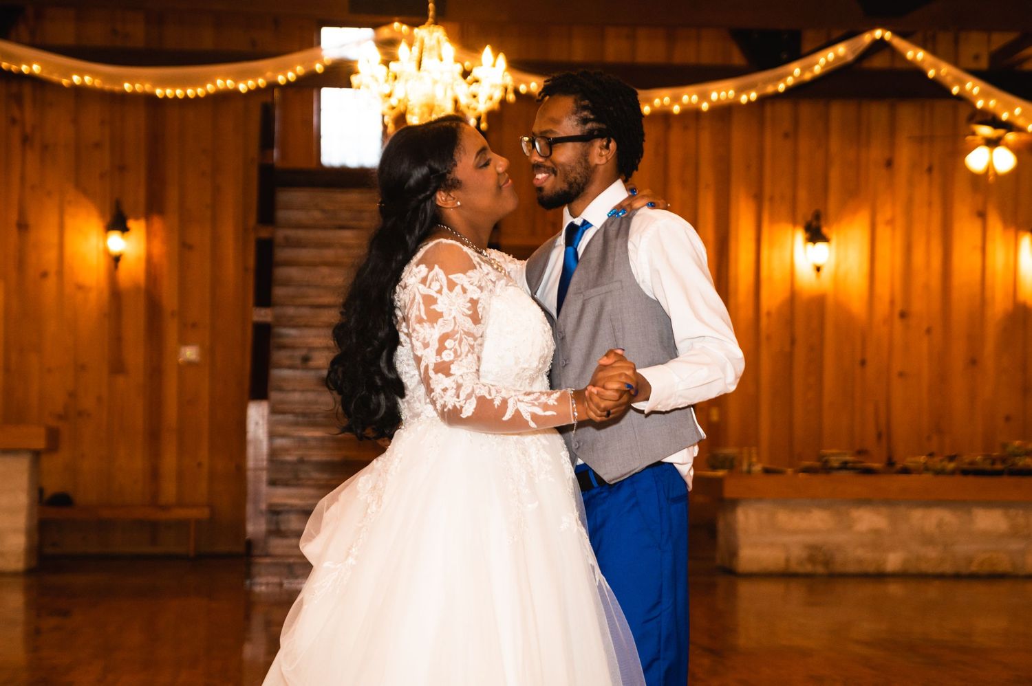 A romantic dance moment captured in a warmly lit wooden reception venue with string lights and decorative draping.