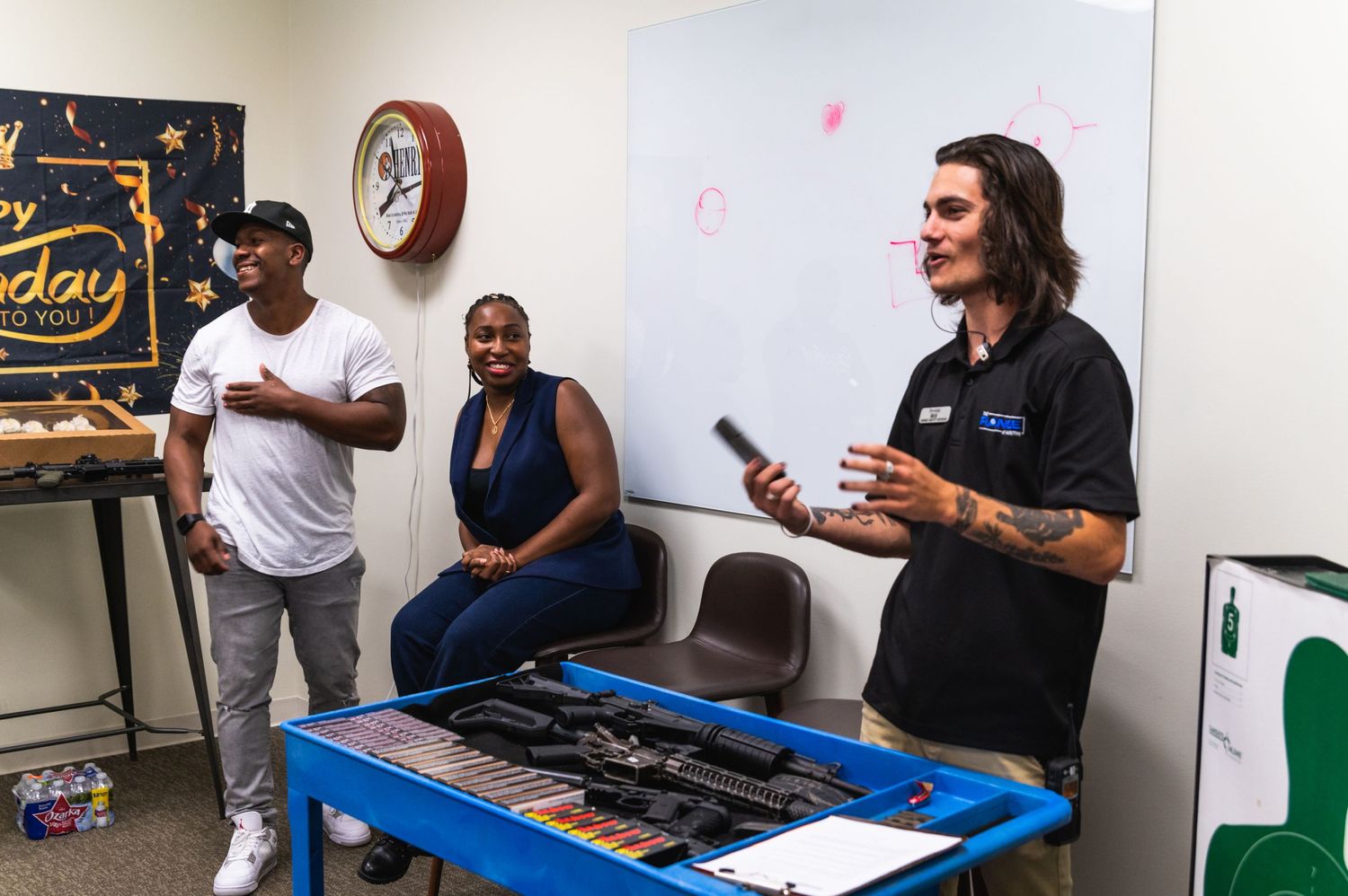An instructor explains firearm safety basics at a training facility with a table of equipment.