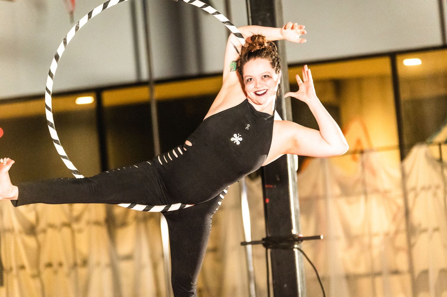 Aerial artist in black attire performs with a hoop under string lights.