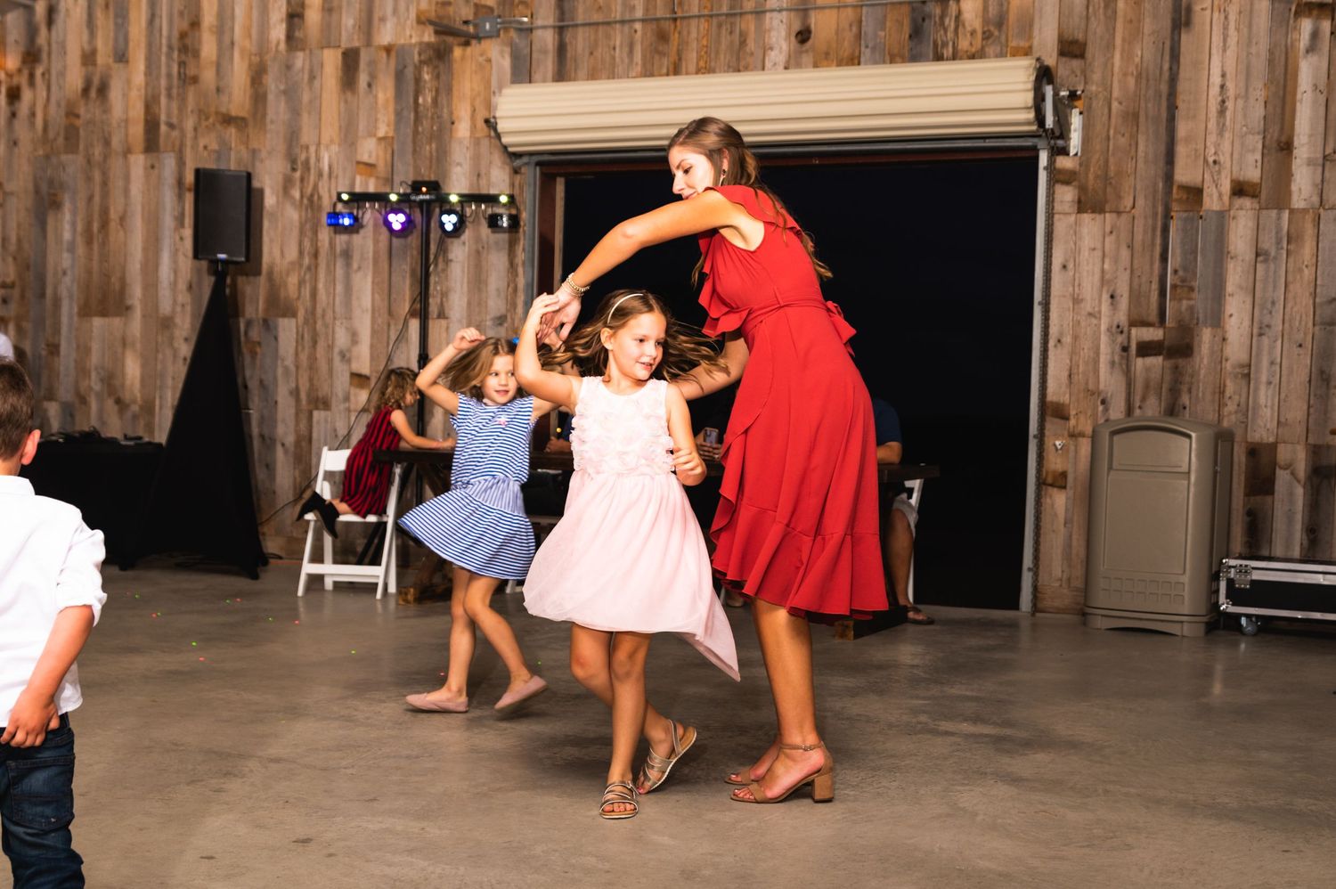People dancing and celebrating at a rustic barn wedding reception with wooden walls.