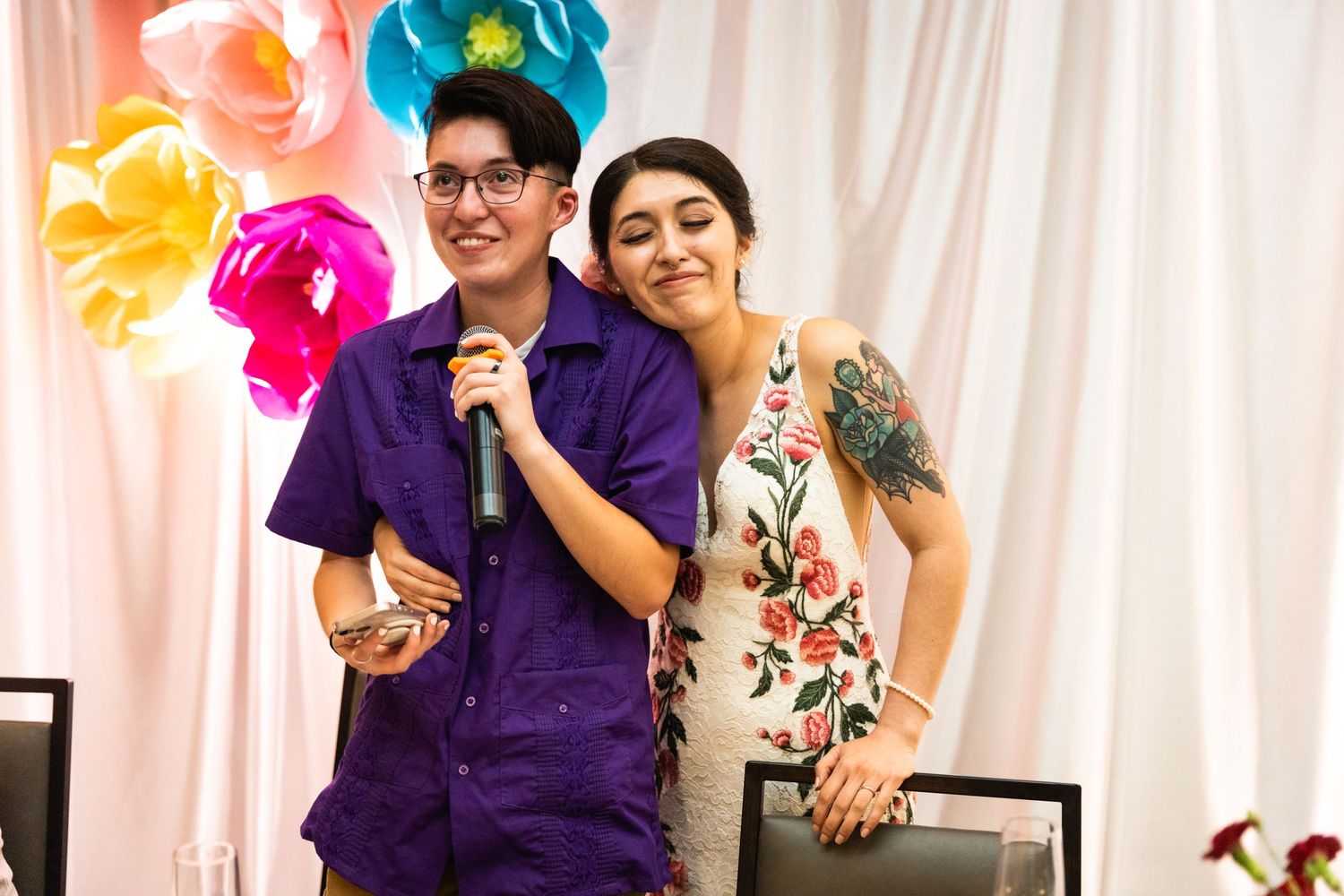 Two people sharing a microphone at a celebration with colorful balloon decorations.