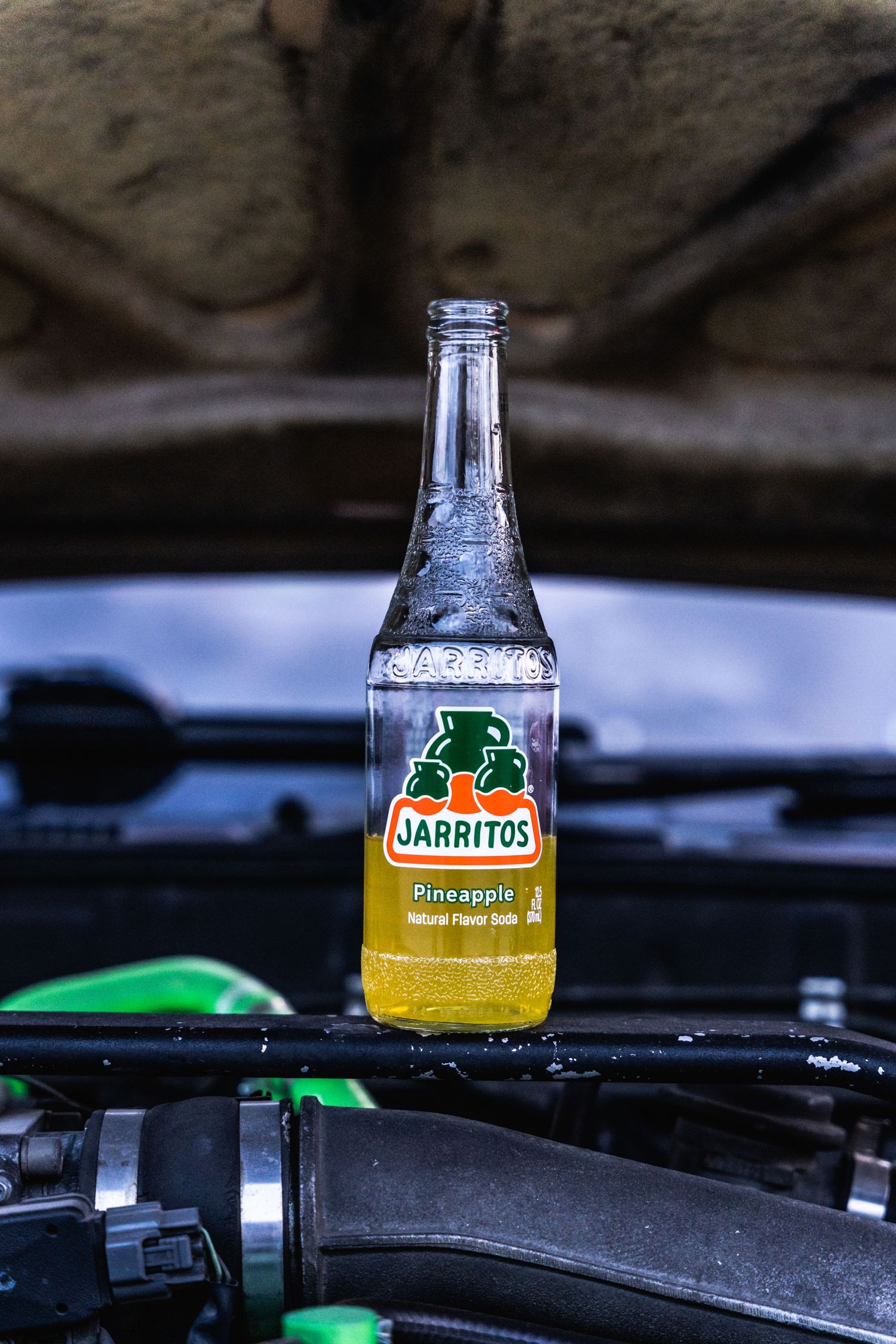A bottle of Jarritos Mexican soda resting on a car's engine bay.