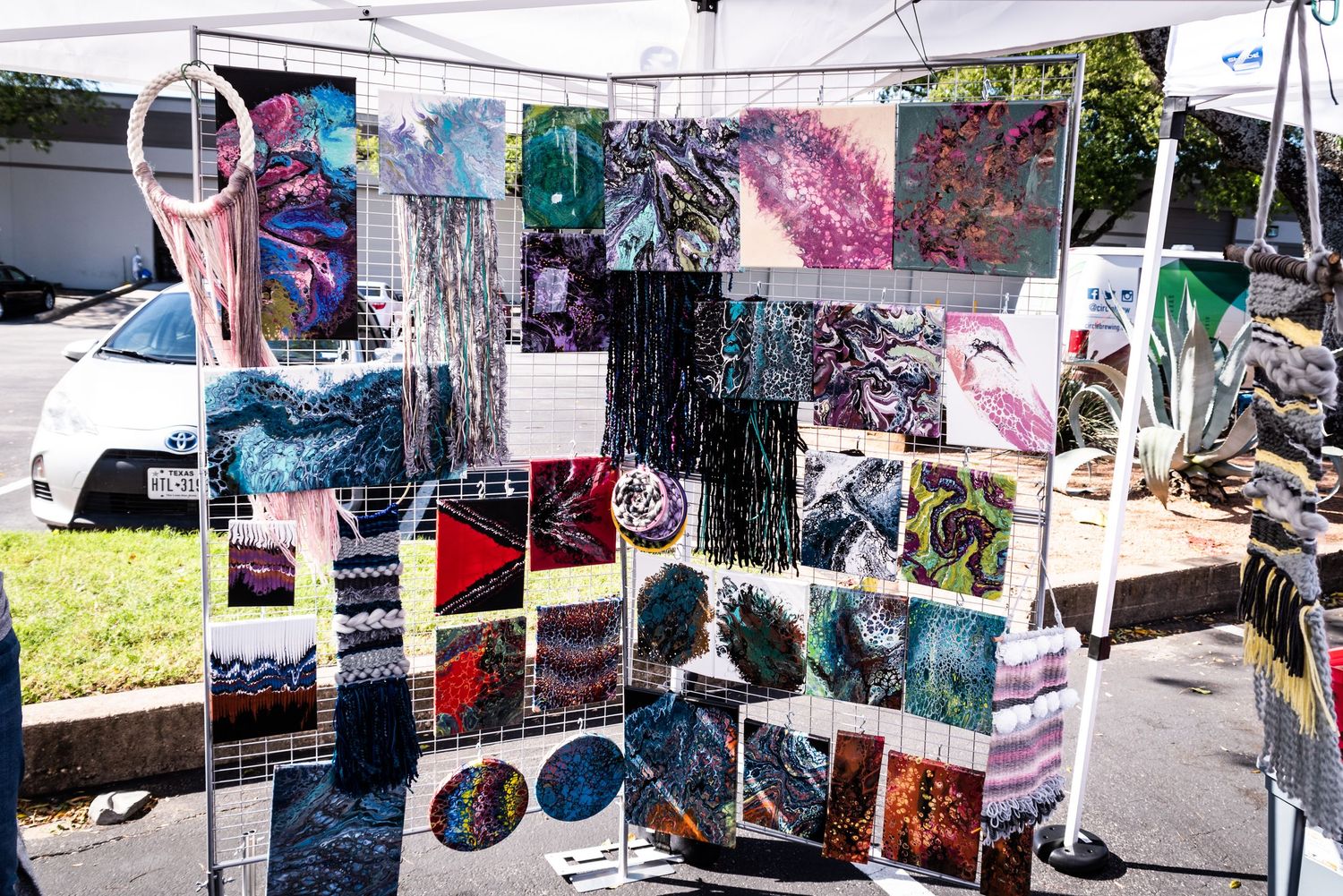 Colorful artwork display at an outdoor market featuring various prints and photographs hanging on display racks.