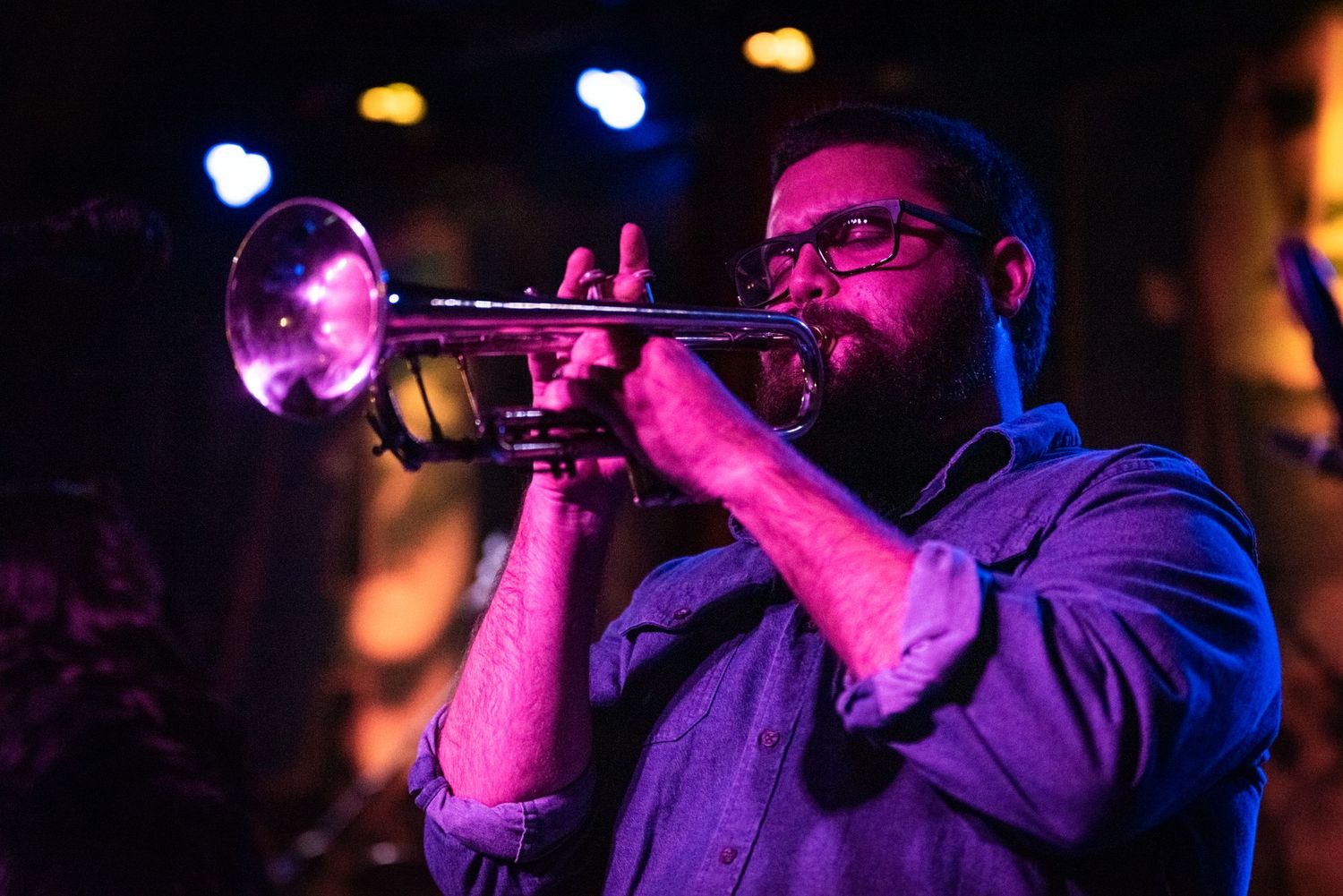 Trumpet player performing passionately under colorful stage lighting at a concert venue.
