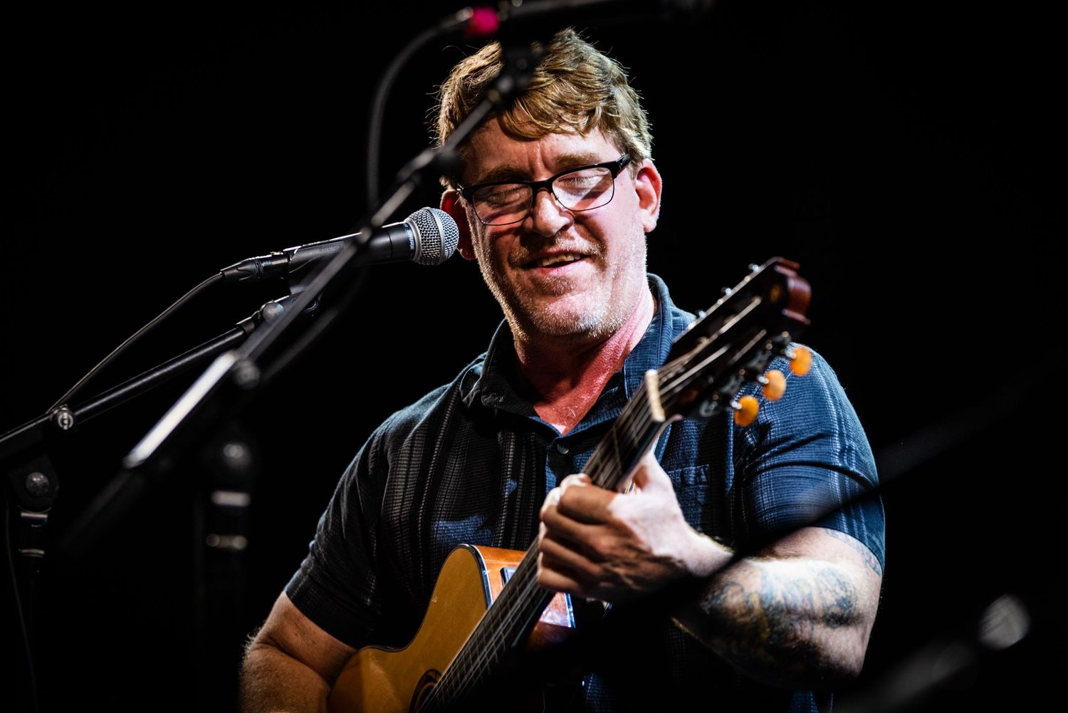 Close-up of performer singing and playing acoustic guitar during live concert.