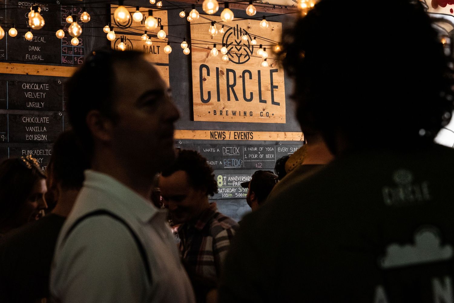 Circle Brewing Company logo illuminated by string lights in dark indoor setting.