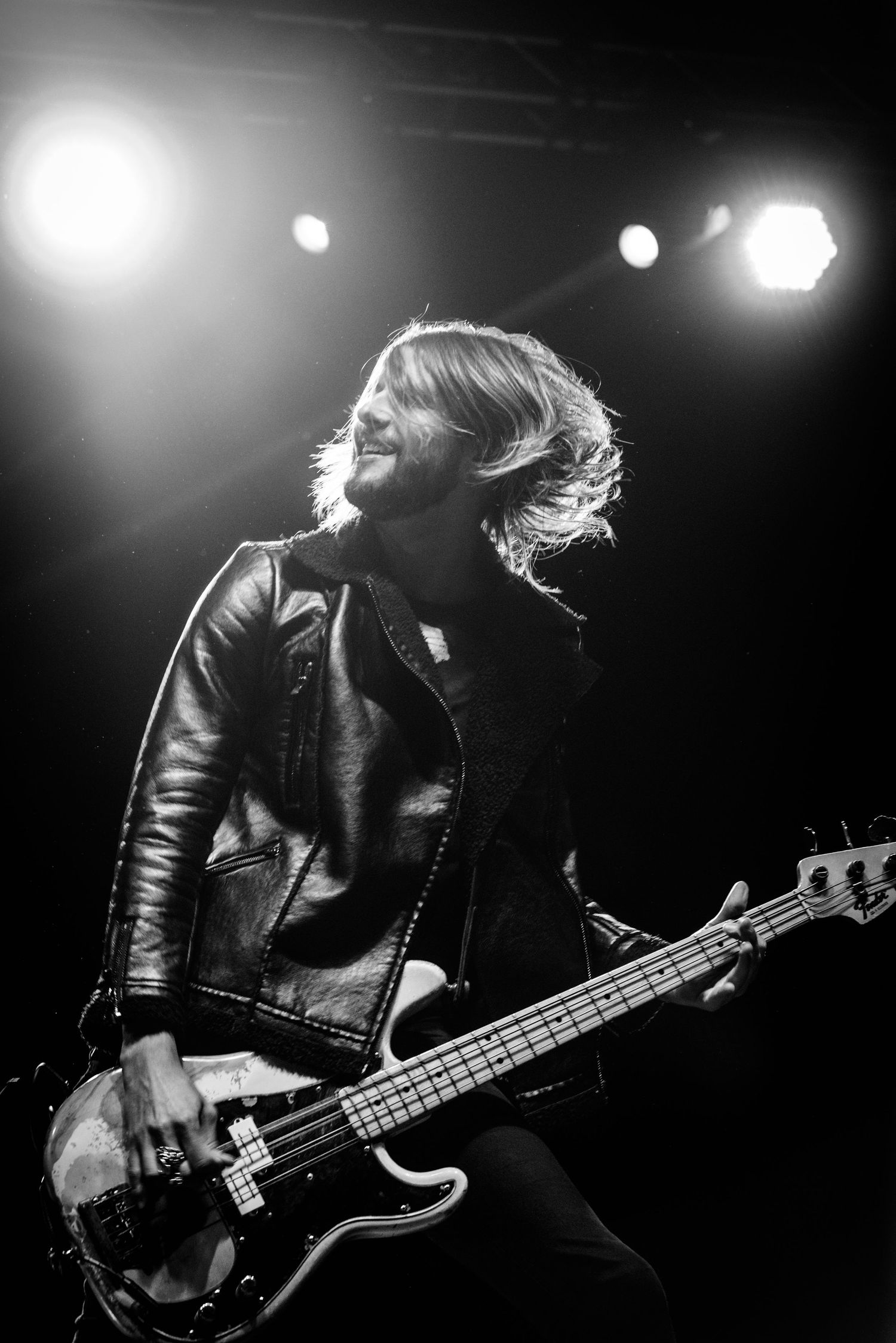 Dynamic black and white photo of bassist playing under dramatic stage lights.