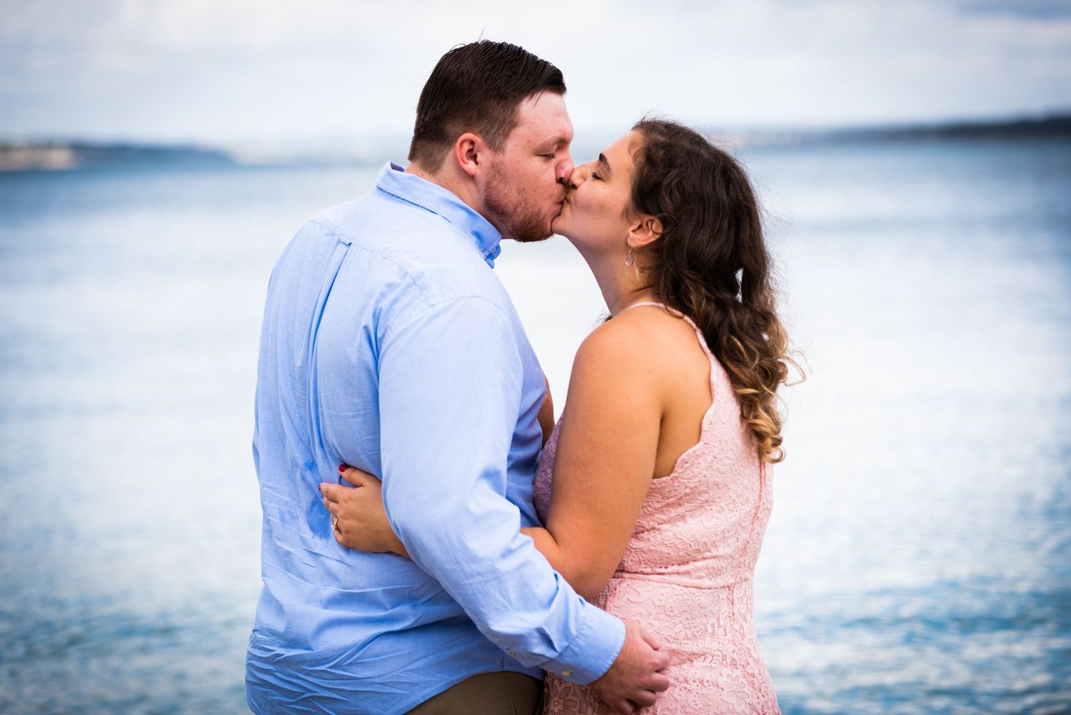 A romantic couple shares a kiss by the ocean at sunset.