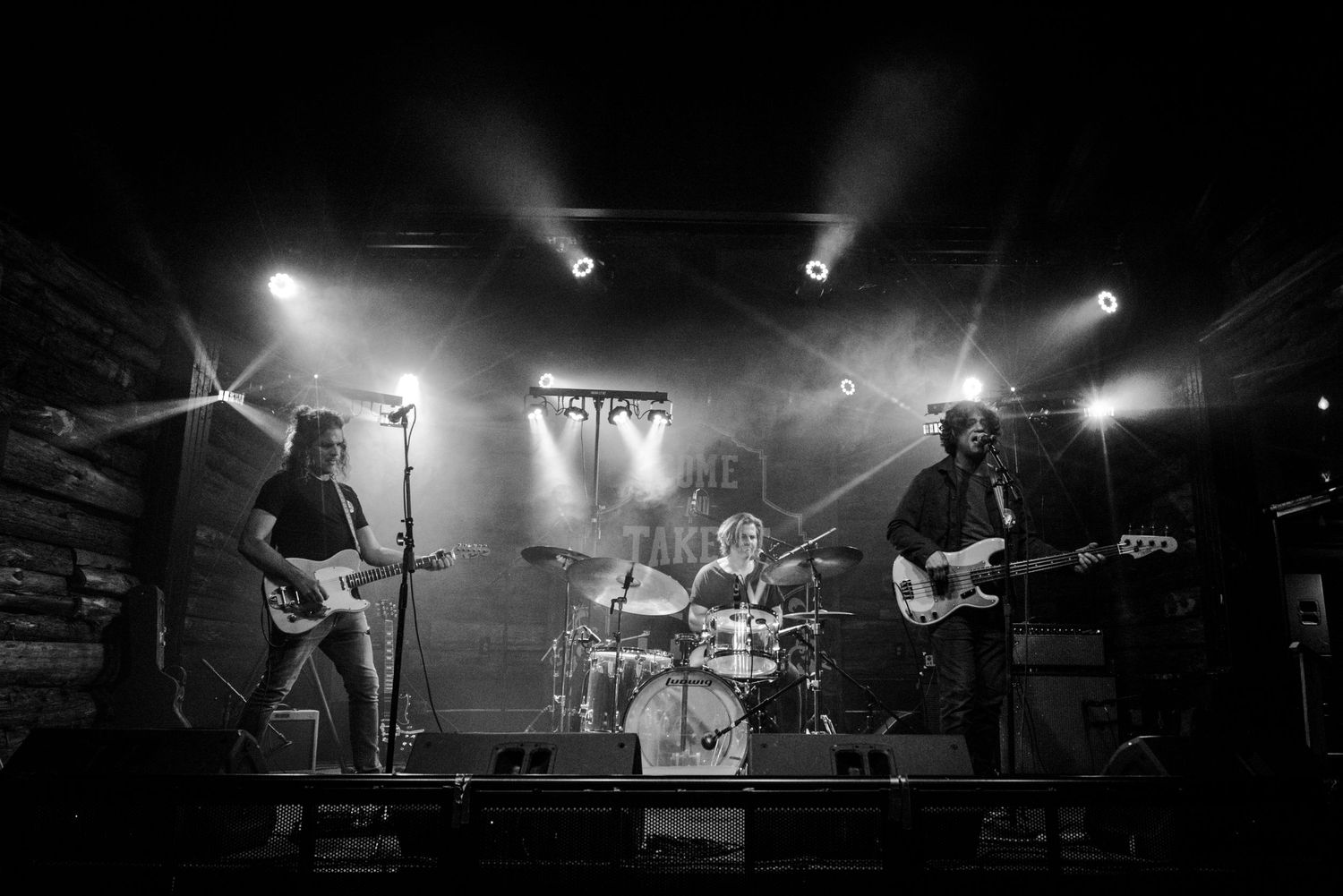 A rock band performs on stage with dramatic backlighting and fog effects.