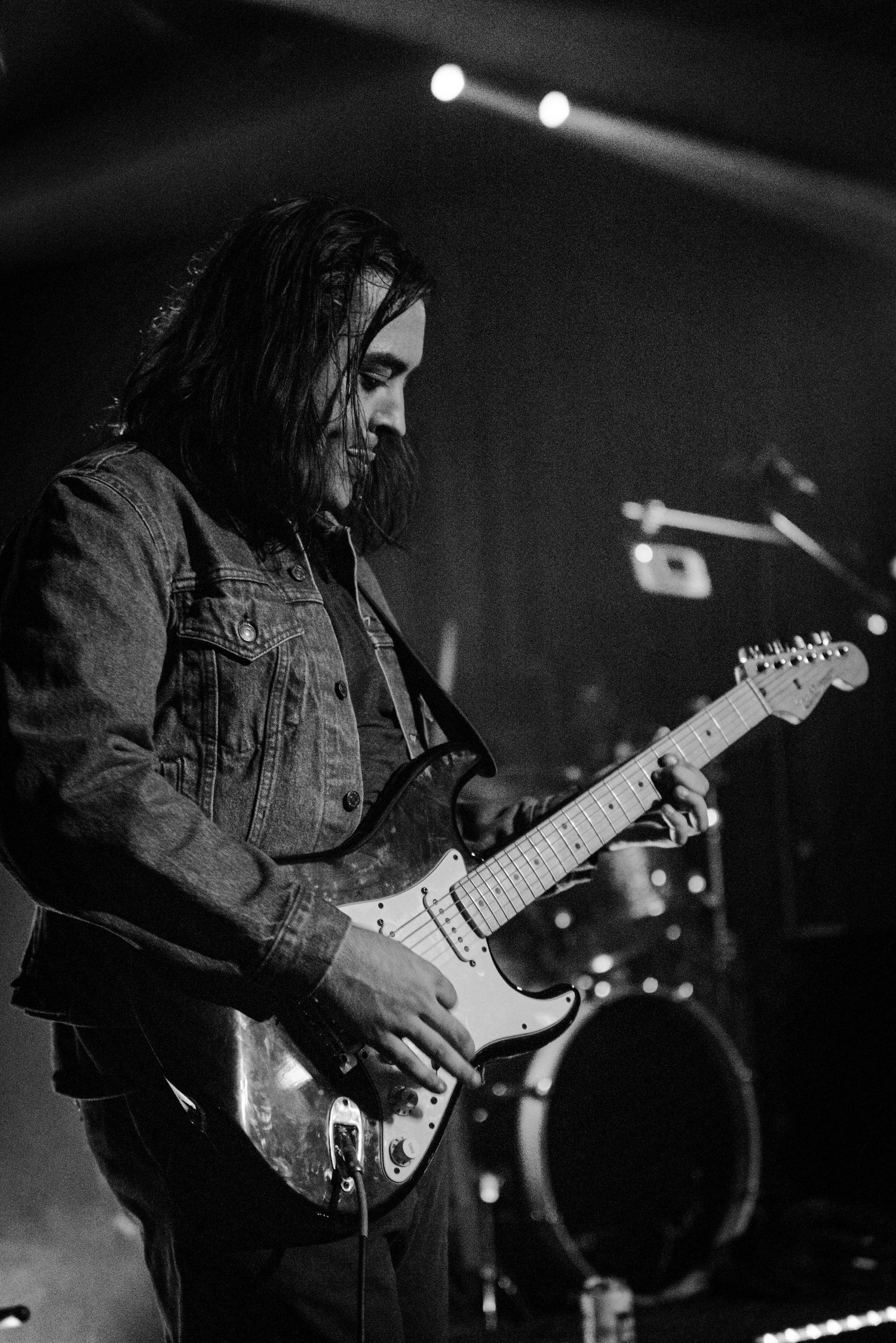 A guitarist wearing a denim jacket performs under dramatic stage lighting.